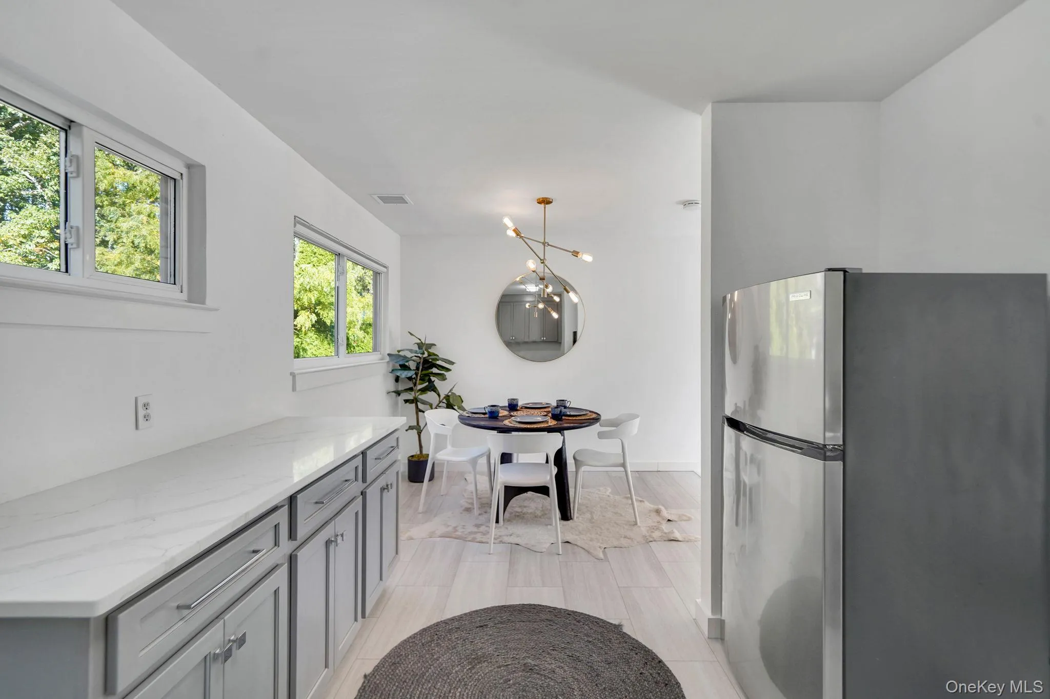 Kitchen with freestanding refrigerator, light stone counters, gray cabinetry, a chandelier, and pendant lighting Kitchen with freestanding refrigerator, light stone counters, gray cabinetry, a chandelier, and pendant lighting