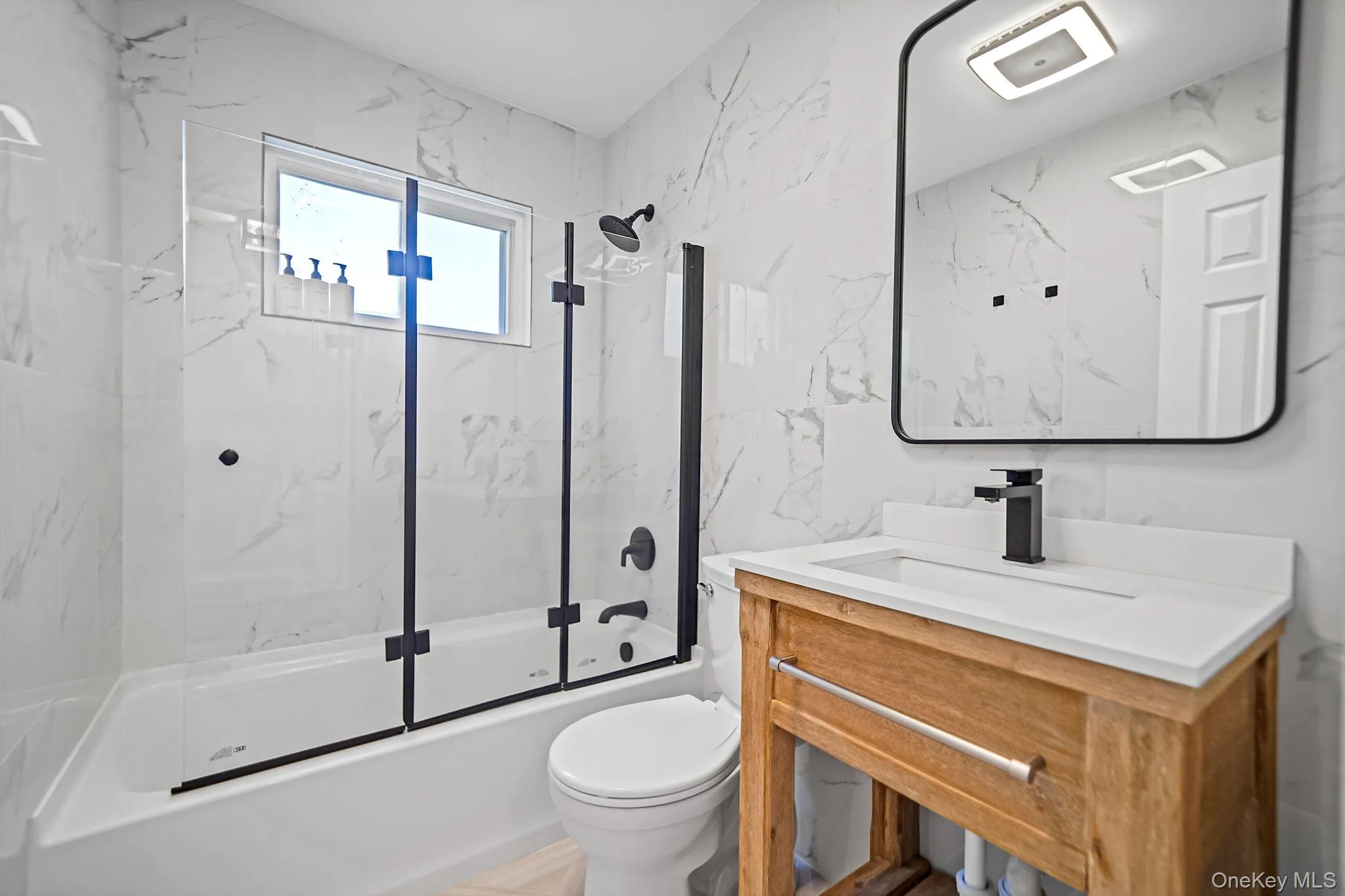 Bathroom featuring bath / shower combo with glass door, vanity, and tile walls Bathroom featuring bath / shower combo with glass door, vanity, and tile walls