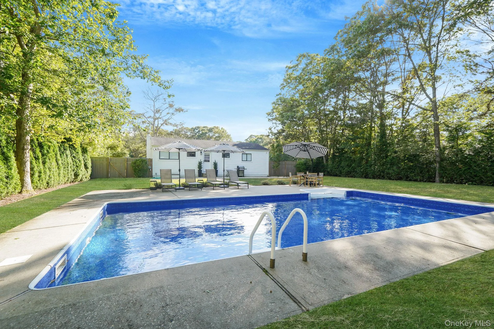 View of swimming pool with a patio area, a fenced backyard, view of scattered trees, and outdoor dining space View of swimming pool with a patio area, a fenced backyard, view of scattered trees, and outdoor dining space