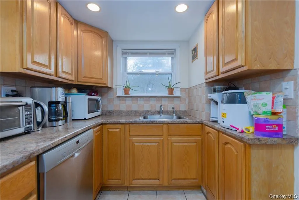 Kitchen featuring tasteful backsplash, stainless steel dishwasher, white microwave, light tile patterned floors, and recessed lighting Kitchen featuring tasteful backsplash, stainless steel dishwasher, white microwave, light tile patterned floors, and recessed lighting