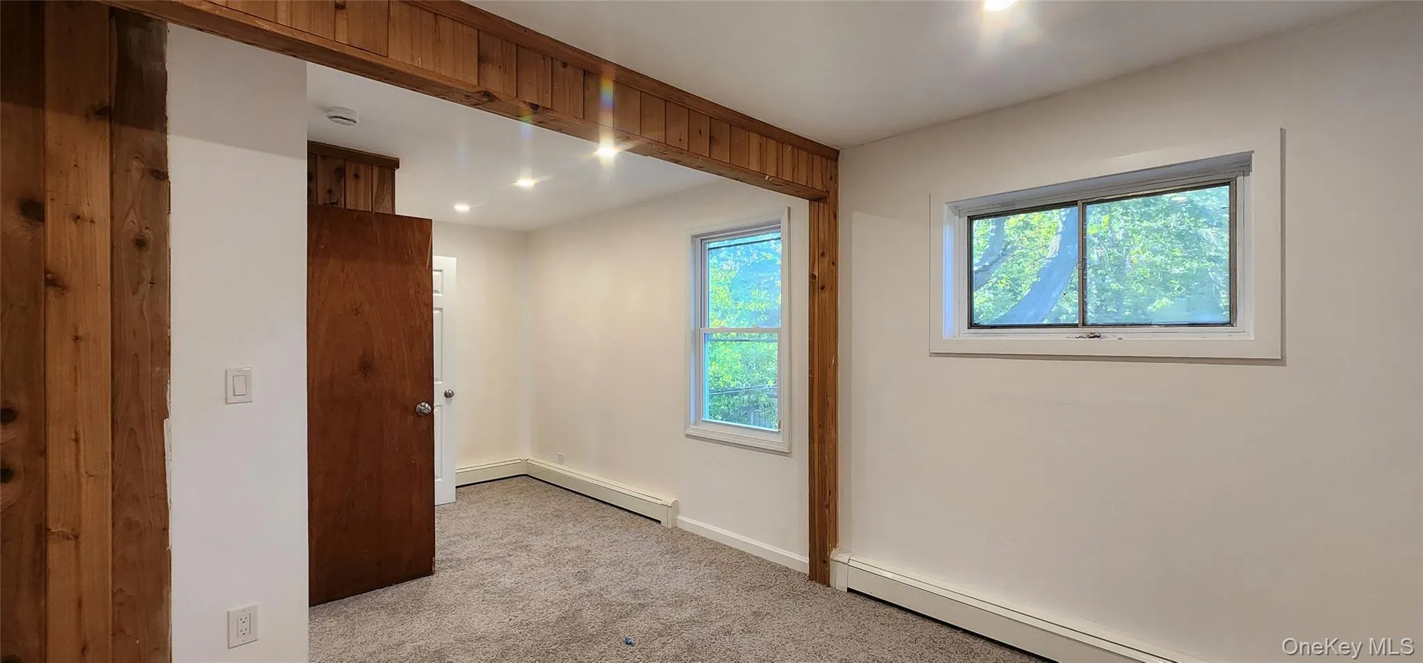 Empty room with plenty of natural light, light colored carpet, a baseboard radiator, and recessed lighting Empty room with plenty of natural light, light colored carpet, a baseboard radiator, and recessed lighting