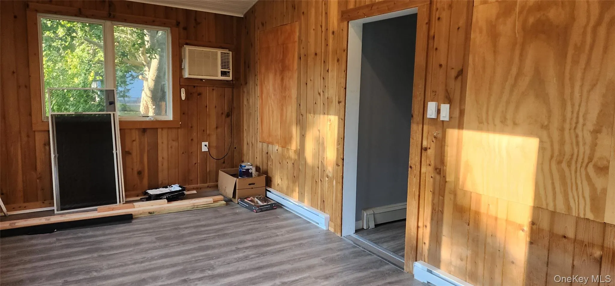 Spare room featuring wooden walls, wood finished floors, a baseboard heating unit, a baseboard radiator, and an AC wall unit Spare room featuring wooden walls, wood finished floors, a baseboard heating unit, a baseboard radiator, and an AC wall unit