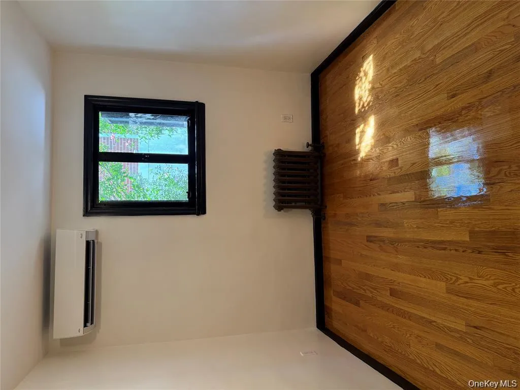 Empty room with radiator heating unit, wood finished floors, and an AC wall unit Empty room with radiator heating unit, wood finished floors, and an AC wall unit