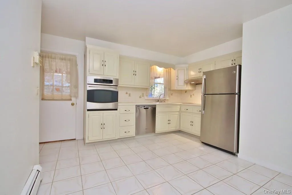 Kitchen featuring stainless steel appliances, light countertops, baseboard heating, decorative backsplash, and cream cabinetry Kitchen featuring stainless steel appliances, light countertops, baseboard heating, decorative backsplash, and cream cabinetry