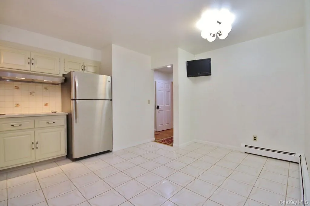 Kitchen with tasteful backsplash, freestanding refrigerator, light countertops, under cabinet range hood, and light tile patterned floors Kitchen with tasteful backsplash, freestanding refrigerator, light countertops, under cabinet range hood, and light tile patterned floors