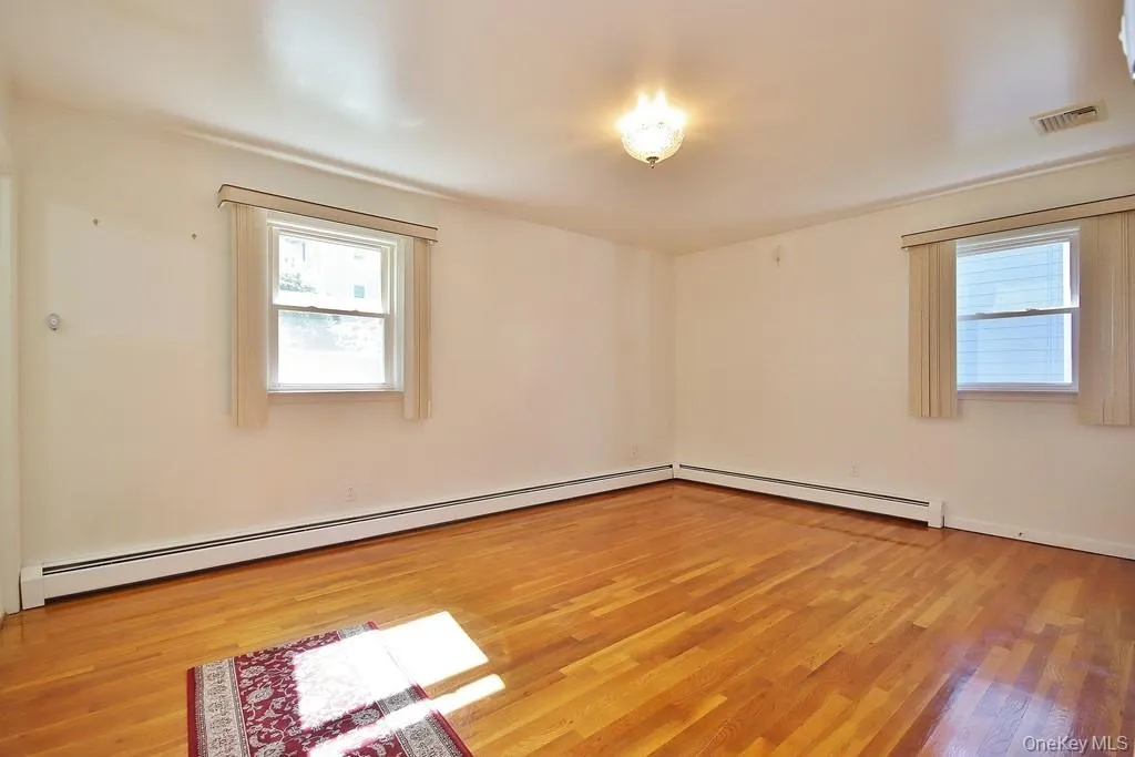 Unfurnished room featuring light wood finished floors and baseboard heating Unfurnished room featuring light wood finished floors and baseboard heating