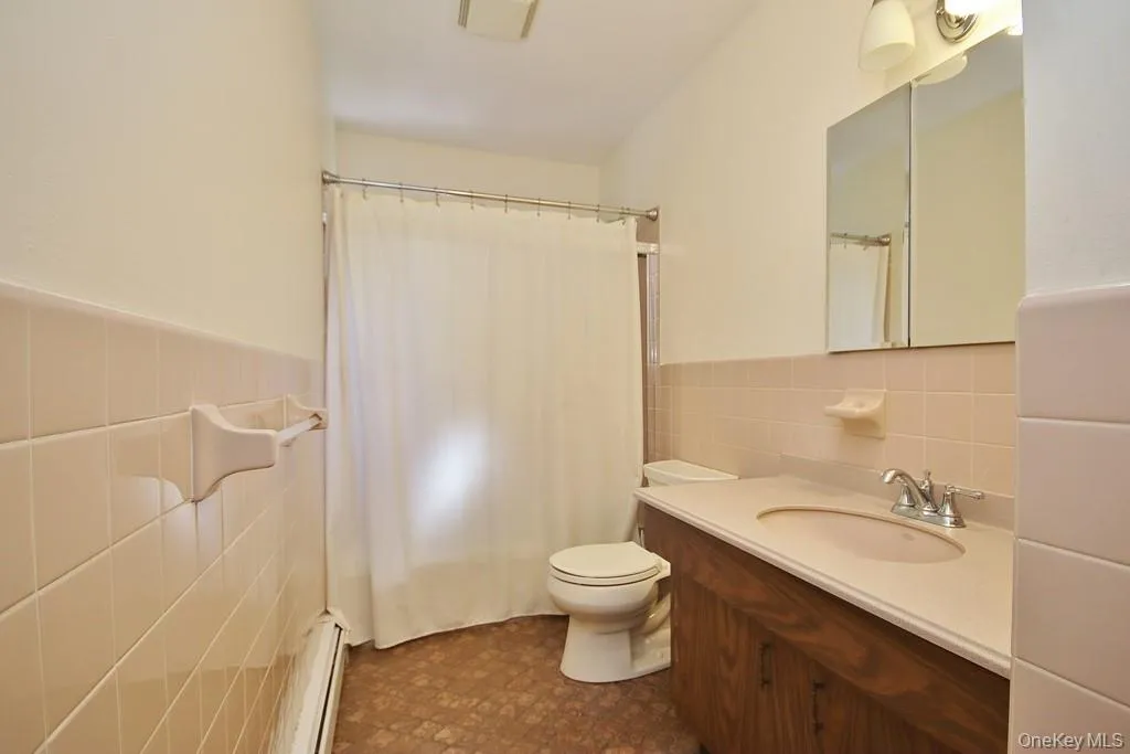 Full bathroom featuring tile walls, vanity, a wainscoted wall, a baseboard radiator, and a shower with shower curtain Full bathroom featuring tile walls, vanity, a wainscoted wall, a baseboard radiator, and a shower with shower curtain
