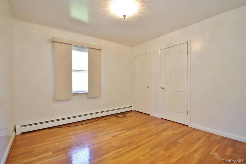 Unfurnished bedroom with baseboard heating, light wood-type flooring, and two closets Unfurnished bedroom with baseboard heating, light wood-type flooring, and two closets