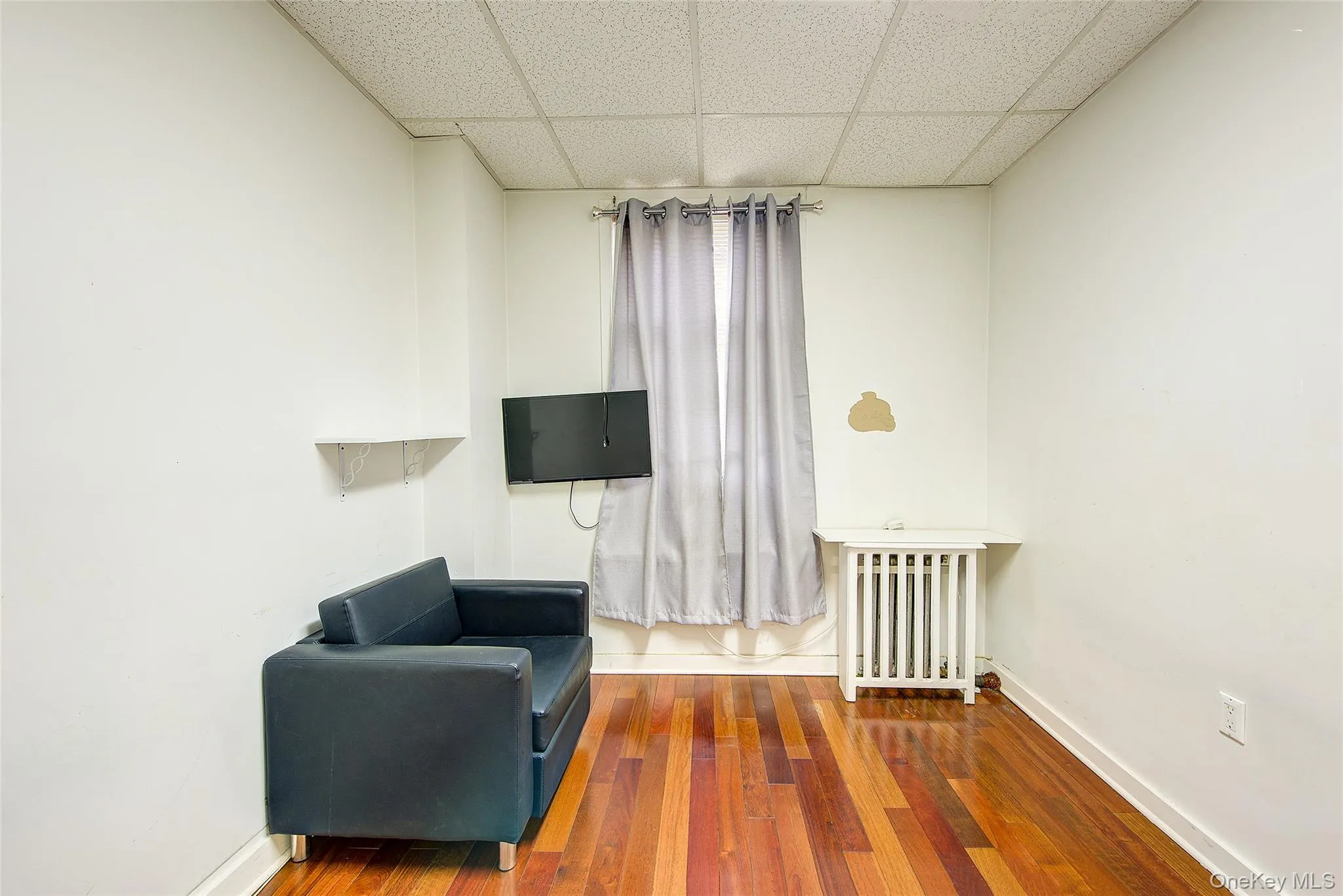 Living area with a paneled ceiling, baseboards, radiator heating unit, and wood-type flooring Living area with a paneled ceiling, baseboards, radiator heating unit, and wood-type flooring