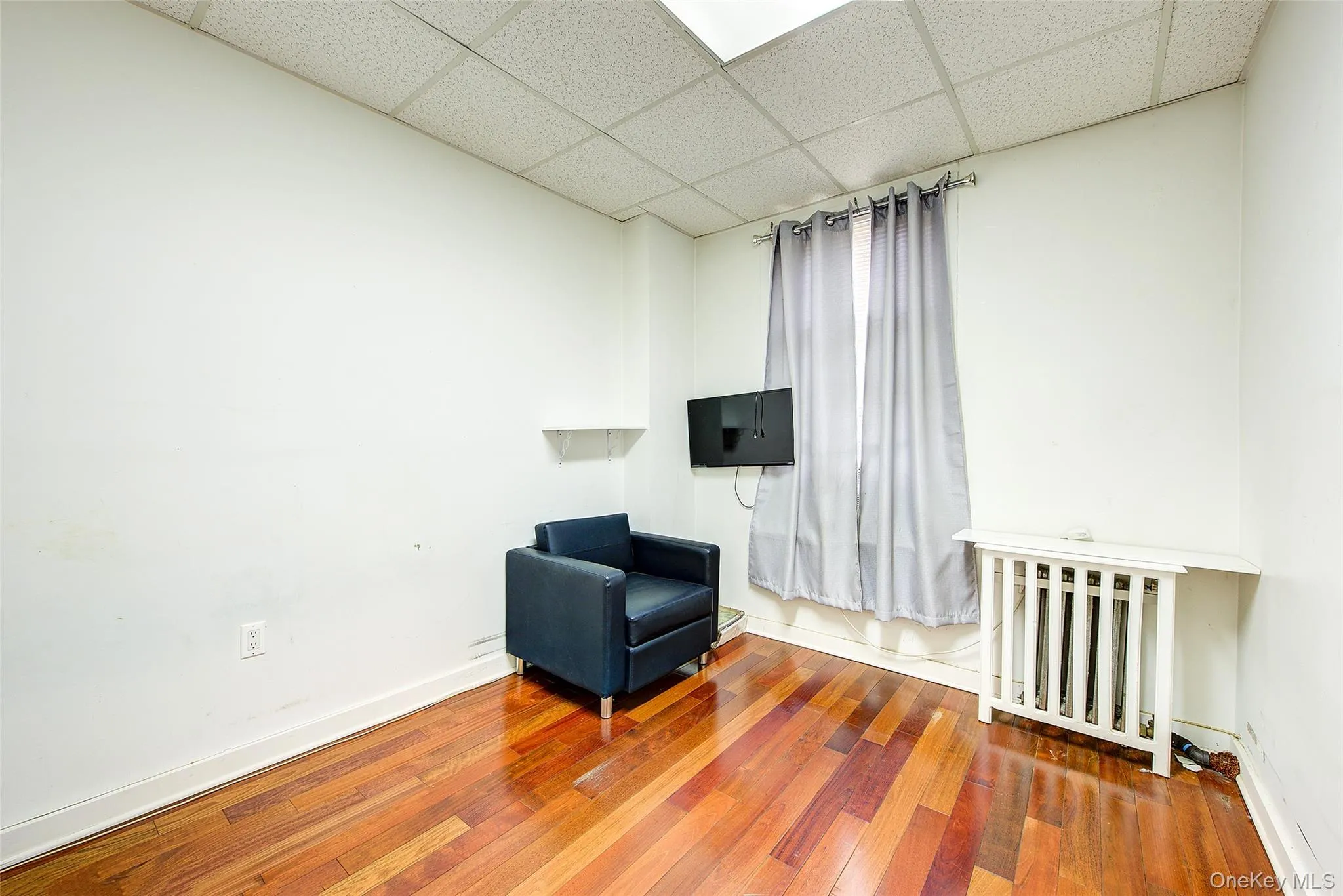 Living area with a paneled ceiling, baseboards, radiator heating unit, and wood-type flooring Living area with a paneled ceiling, baseboards, radiator heating unit, and wood-type flooring