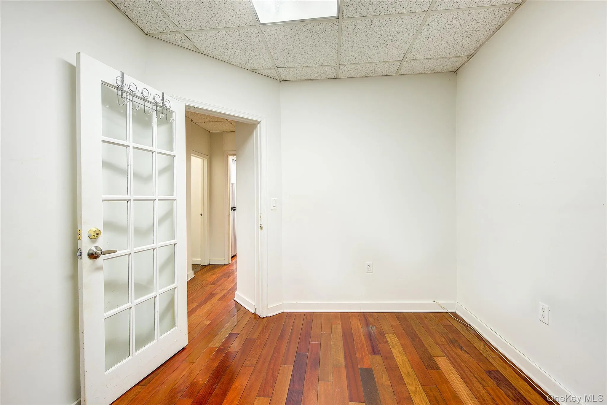 Unfurnished room featuring baseboards, wood-type flooring, and a paneled ceiling Unfurnished room featuring baseboards, wood-type flooring, and a paneled ceiling
