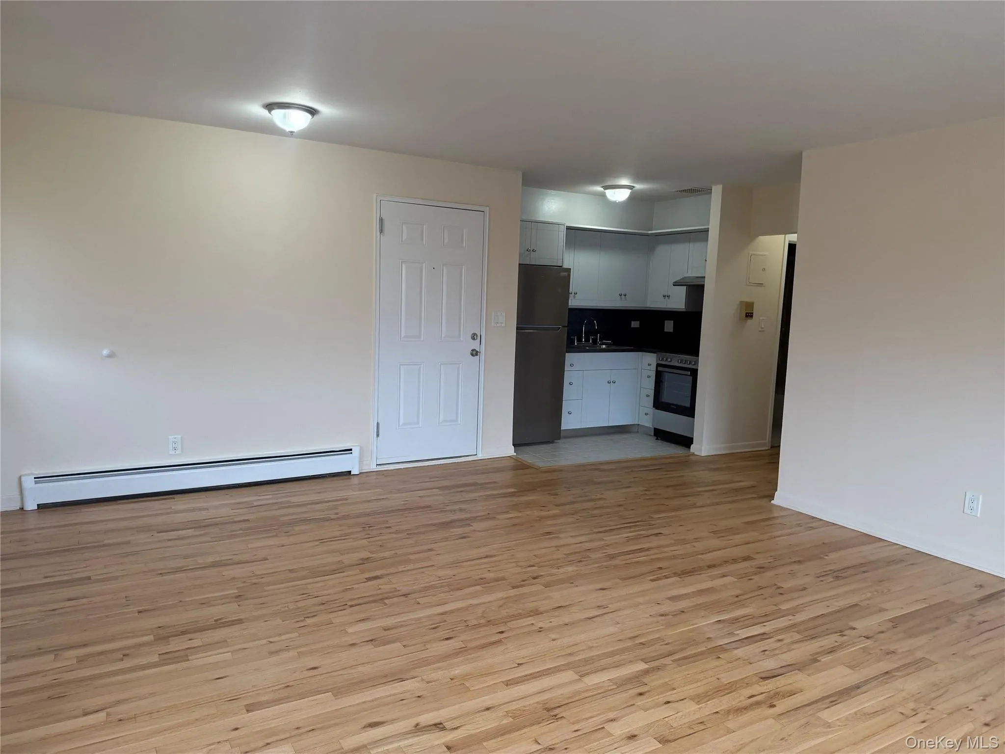 Unfurnished living room with baseboard heating and light wood-style flooring Unfurnished living room with baseboard heating and light wood-style flooring