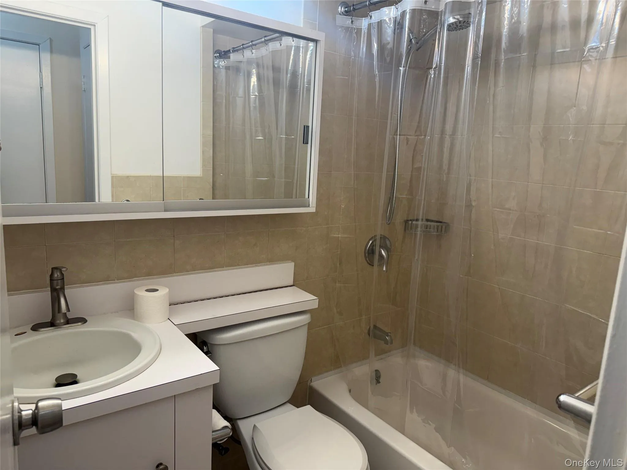 Bathroom featuring shower / bath combo with shower curtain, vanity, tile walls, and decorative backsplash Bathroom featuring shower / bath combo with shower curtain, vanity, tile walls, and decorative backsplash