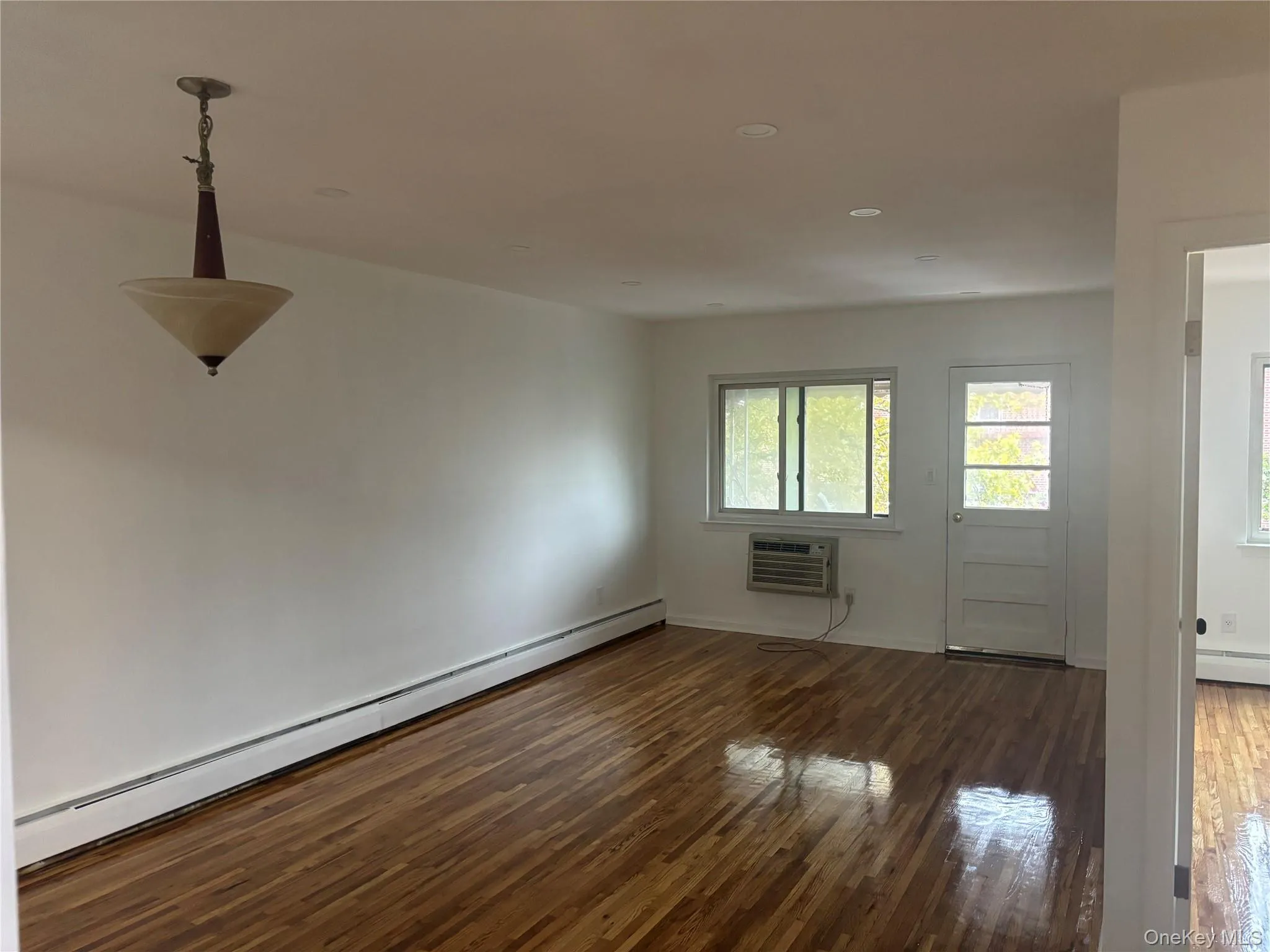 Empty room with a baseboard radiator, dark wood-style floors, recessed lighting, and a wall mounted AC Empty room with a baseboard radiator, dark wood-style floors, recessed lighting, and a wall mounted AC