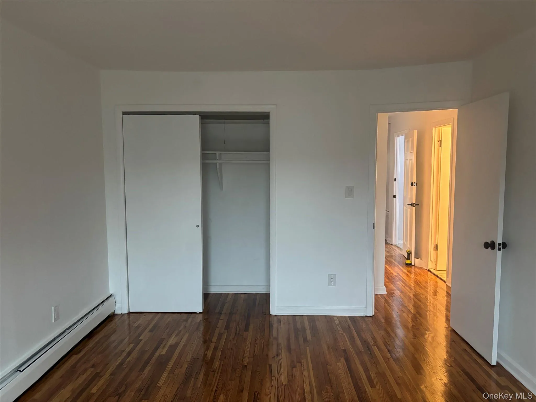 Unfurnished bedroom featuring a baseboard radiator, dark wood-style floors, and a closet Unfurnished bedroom featuring a baseboard radiator, dark wood-style floors, and a closet