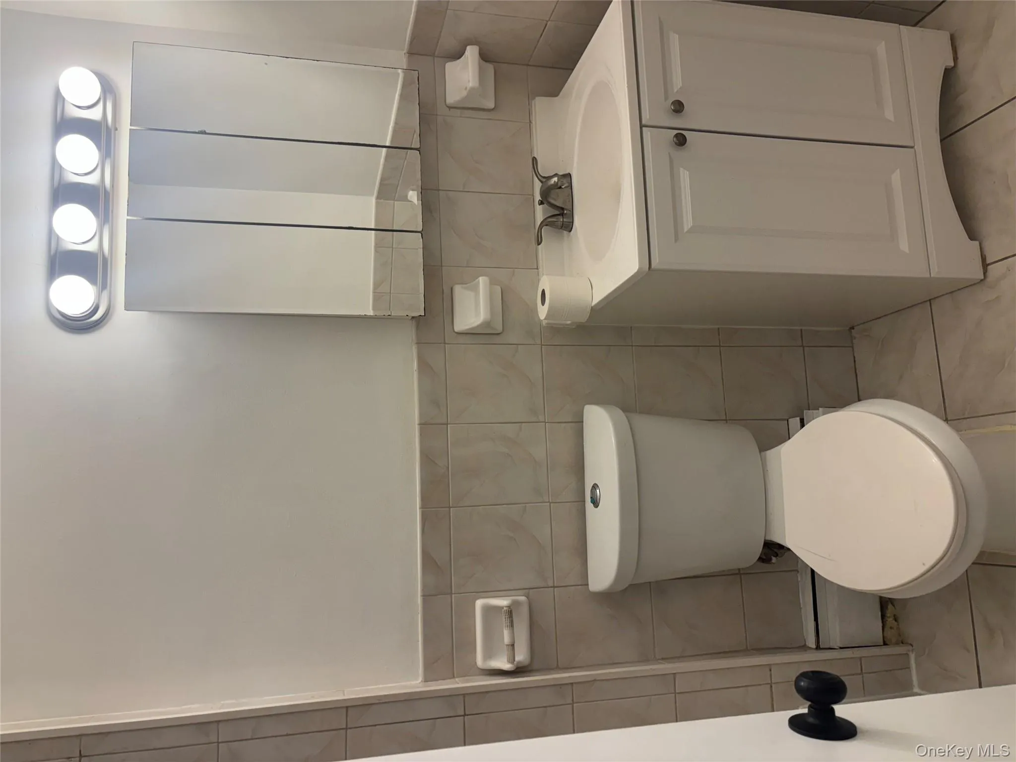 Bathroom with tile walls, vanity, a wainscoted wall, light tile patterned floors, and a baseboard radiator Bathroom with tile walls, vanity, a wainscoted wall, light tile patterned floors, and a baseboard radiator