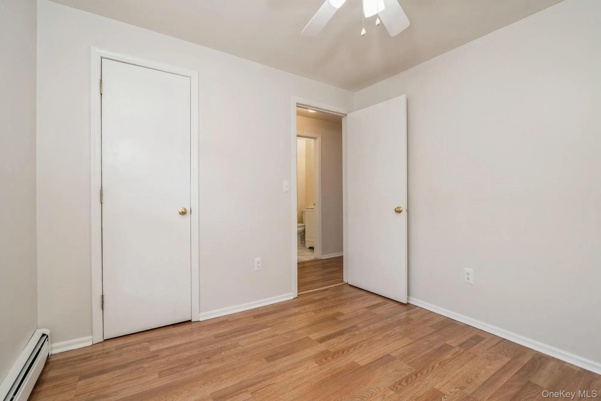 Unfurnished bedroom featuring baseboard heating, wood finished floors, and a ceiling fan Unfurnished bedroom featuring baseboard heating, wood finished floors, and a ceiling fan