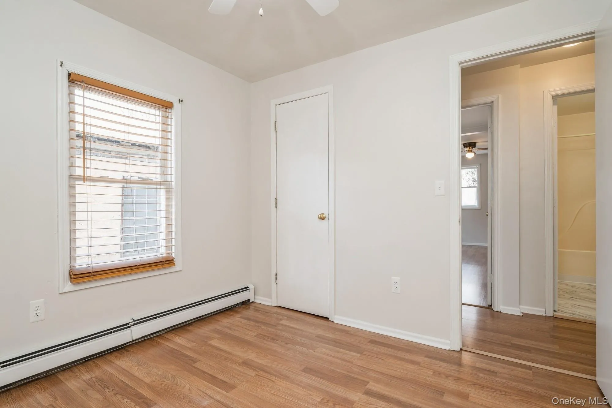 Unfurnished bedroom with baseboard heating, light wood-type flooring, and ceiling fan Unfurnished bedroom with baseboard heating, light wood-type flooring, and ceiling fan