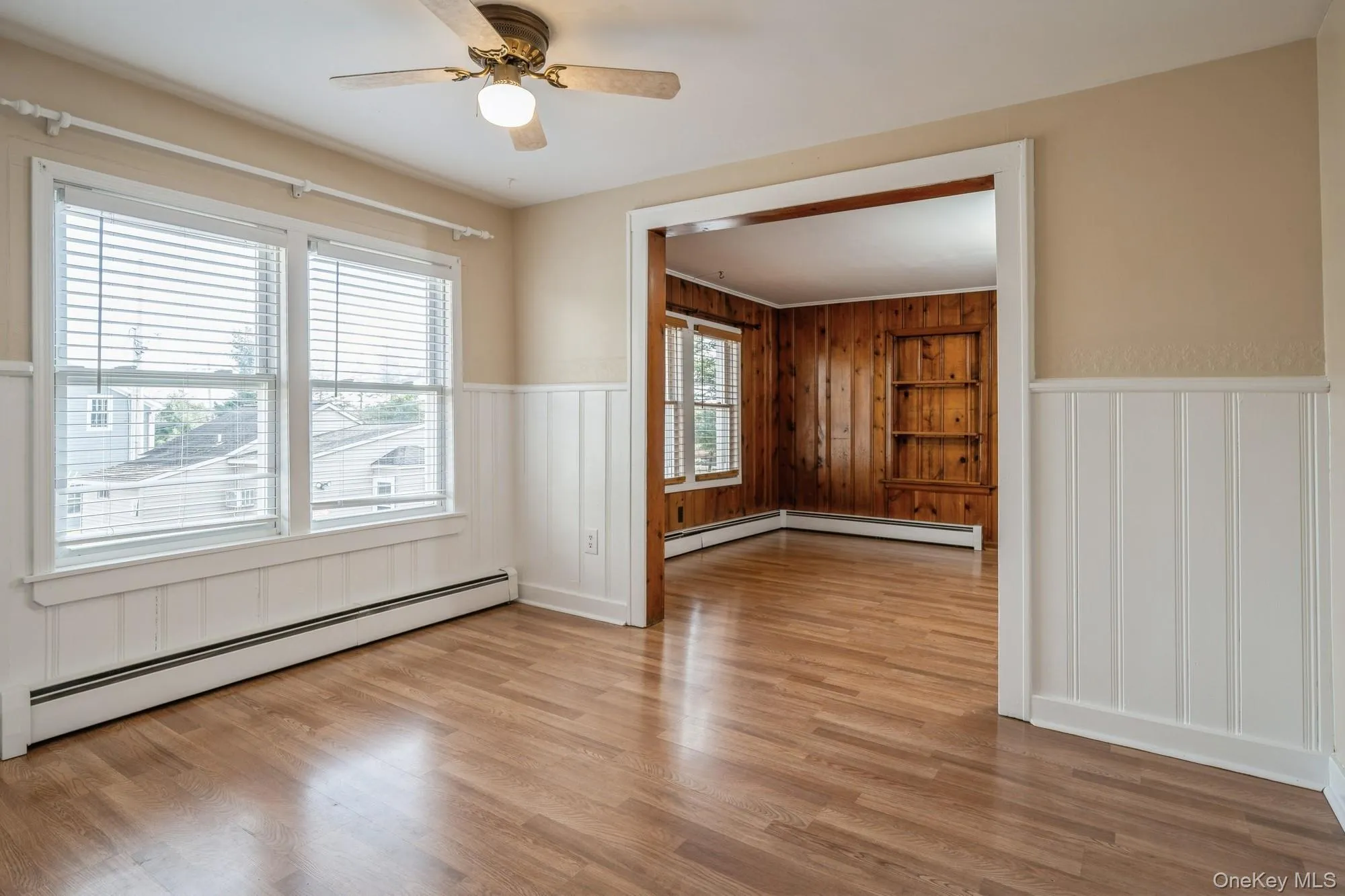 Dining room featuring wainscoting, baseboard heating, light wood-style flooring, a ceiling fan, and a decorative wall Dining room featuring wainscoting, baseboard heating, light wood-style flooring, a ceiling fan, and a decorative wall