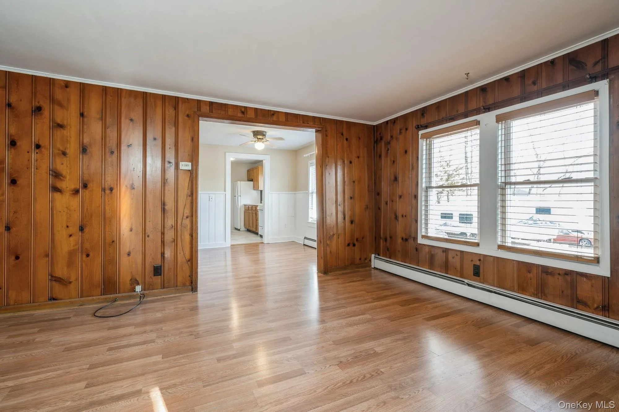 Living room with wooden walls, light wood-style floors, ornamental molding, a baseboard heating unit, and a ceiling fan Living room with wooden walls, light wood-style floors, ornamental molding, a baseboard heating unit, and a ceiling fan