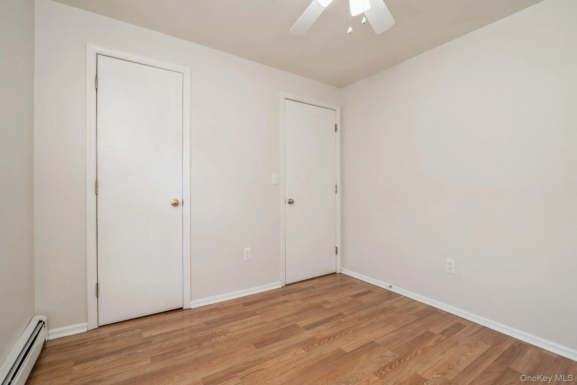 Unfurnished bedroom featuring a baseboard radiator, wood finished floors, and a ceiling fan Unfurnished bedroom featuring a baseboard radiator, wood finished floors, and a ceiling fan
