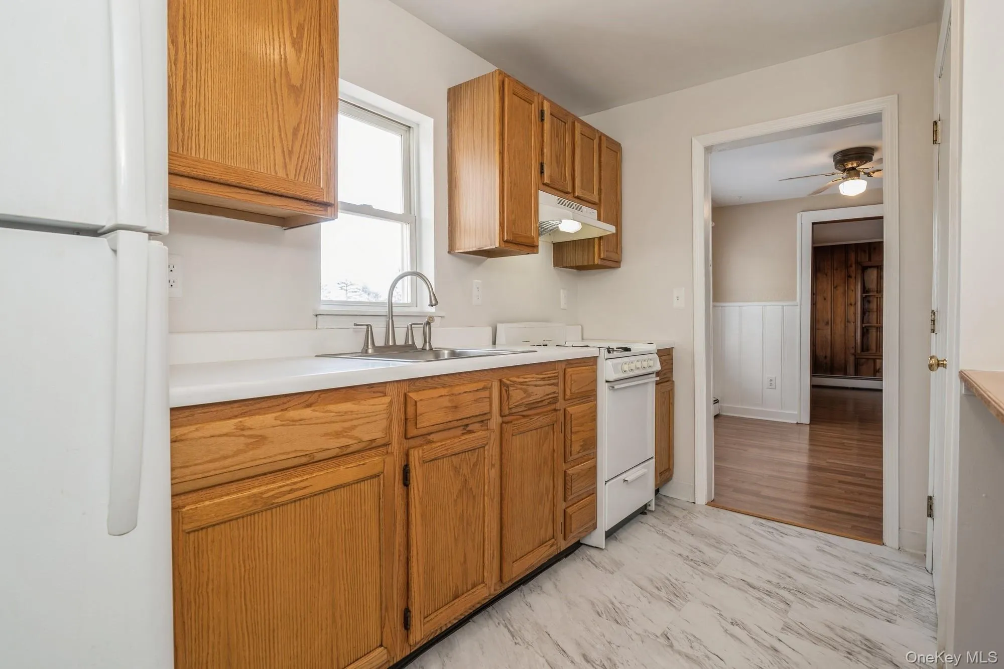 Kitchen with white appliances, light countertops, under cabinet range hood, brown cabinets, and ceiling fan Kitchen with white appliances, light countertops, under cabinet range hood, brown cabinets, and ceiling fan