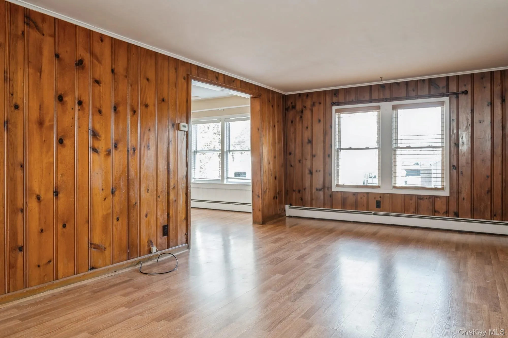 Living room featuring wood walls, wood finished floors, a baseboard heating unit, and ornamental molding Living room featuring wood walls, wood finished floors, a baseboard heating unit, and ornamental molding