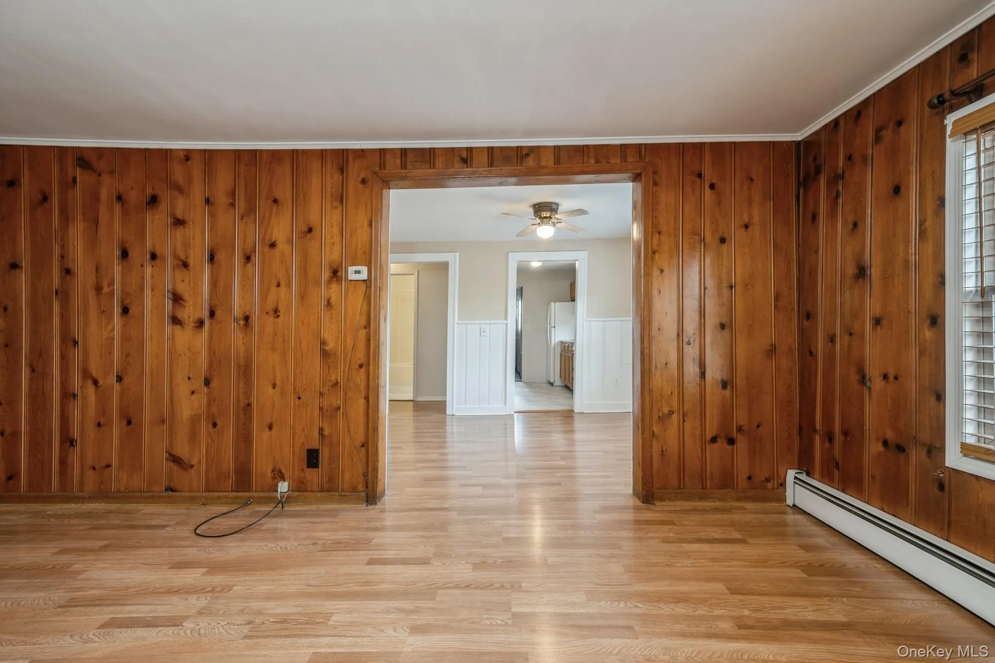 Living room featuring a baseboard heating unit, light wood-style flooring, wood walls, and ceiling fan Living room featuring a baseboard heating unit, light wood-style flooring, wood walls, and ceiling fan