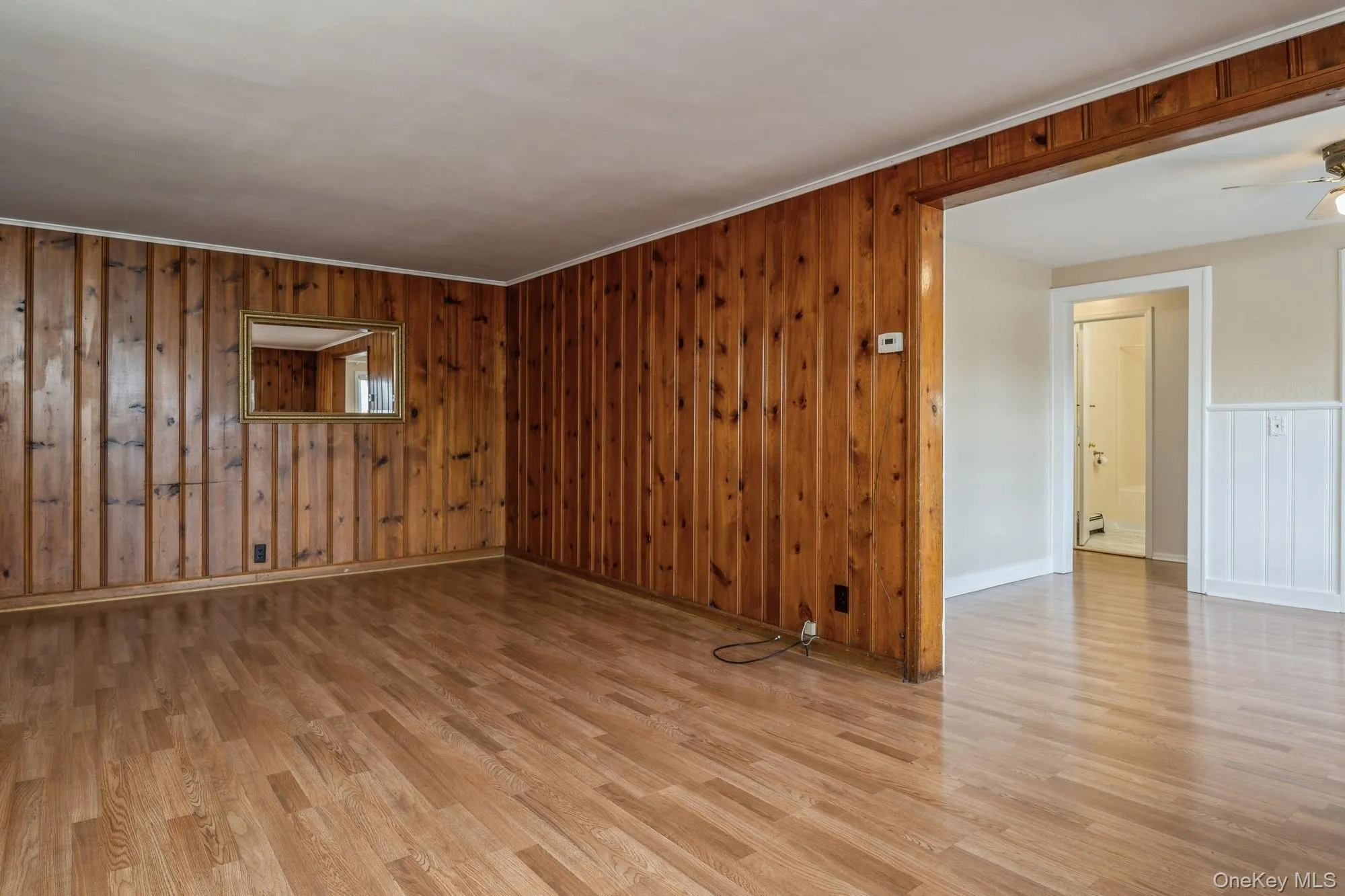 Living room with light wood finished floors, wood walls, ceiling fan, a decorative wall, and ornamental molding Living room with light wood finished floors, wood walls, ceiling fan, a decorative wall, and ornamental molding