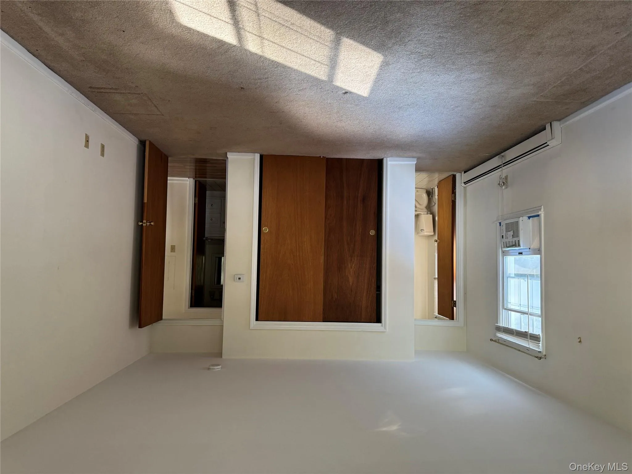Unfurnished bedroom with a baseboard radiator, light carpet, a closet, cooling unit, and ensuite bath Unfurnished bedroom with a baseboard radiator, light carpet, a closet, cooling unit, and ensuite bath