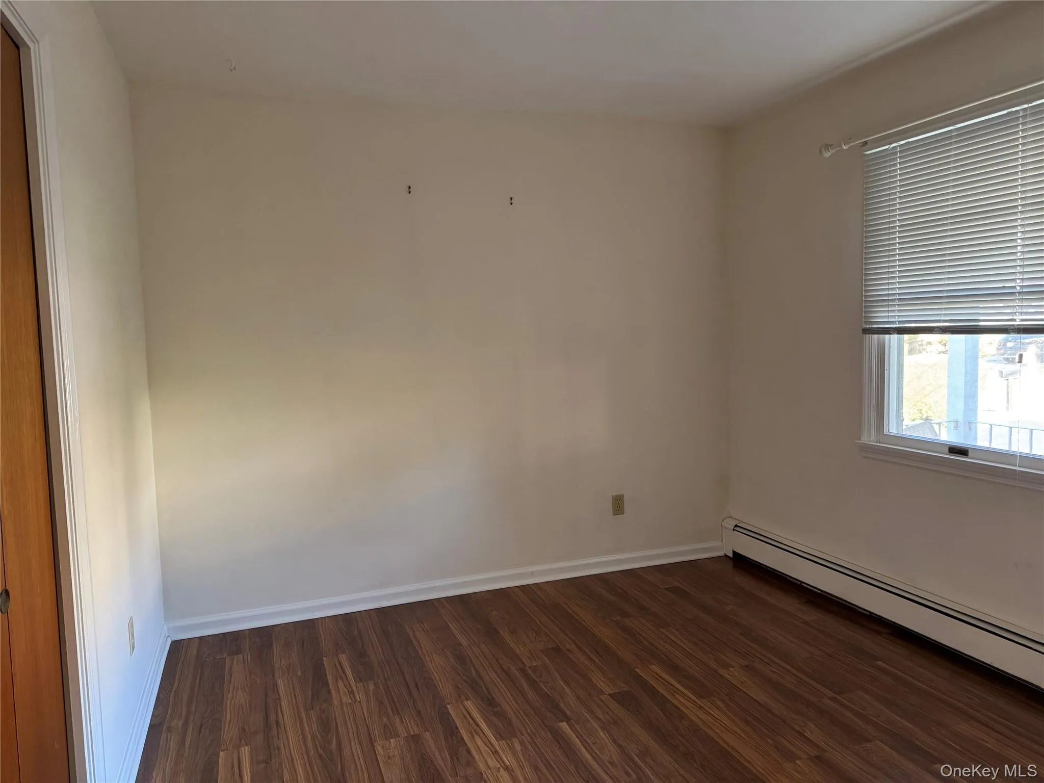 Unfurnished room featuring dark wood-style floors and a baseboard radiator Unfurnished room featuring dark wood-style floors and a baseboard radiator