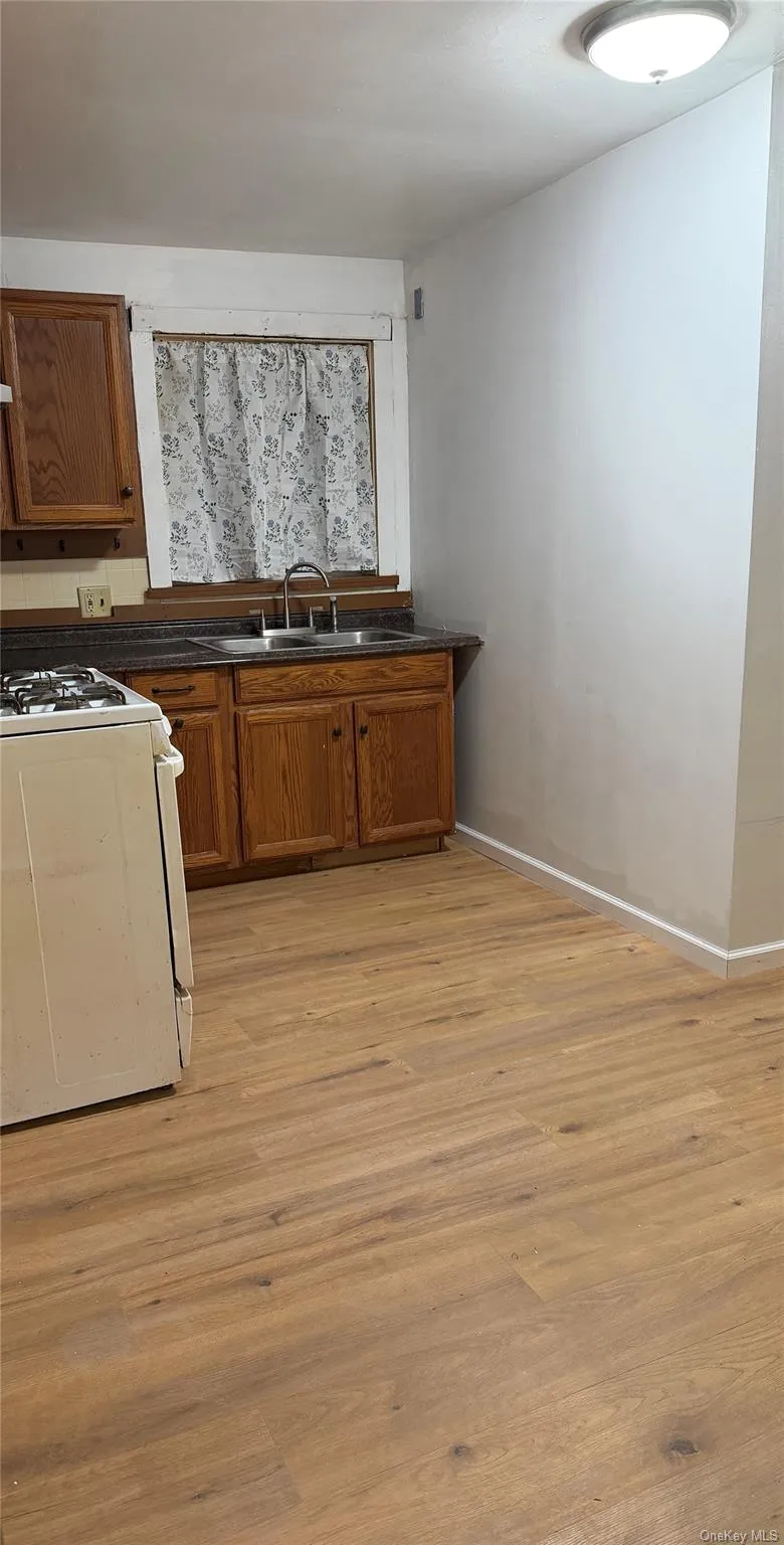 Kitchen with white gas stove, brown cabinets, dark countertops, and light wood finished floors Kitchen with white gas stove, brown cabinets, dark countertops, and light wood finished floors