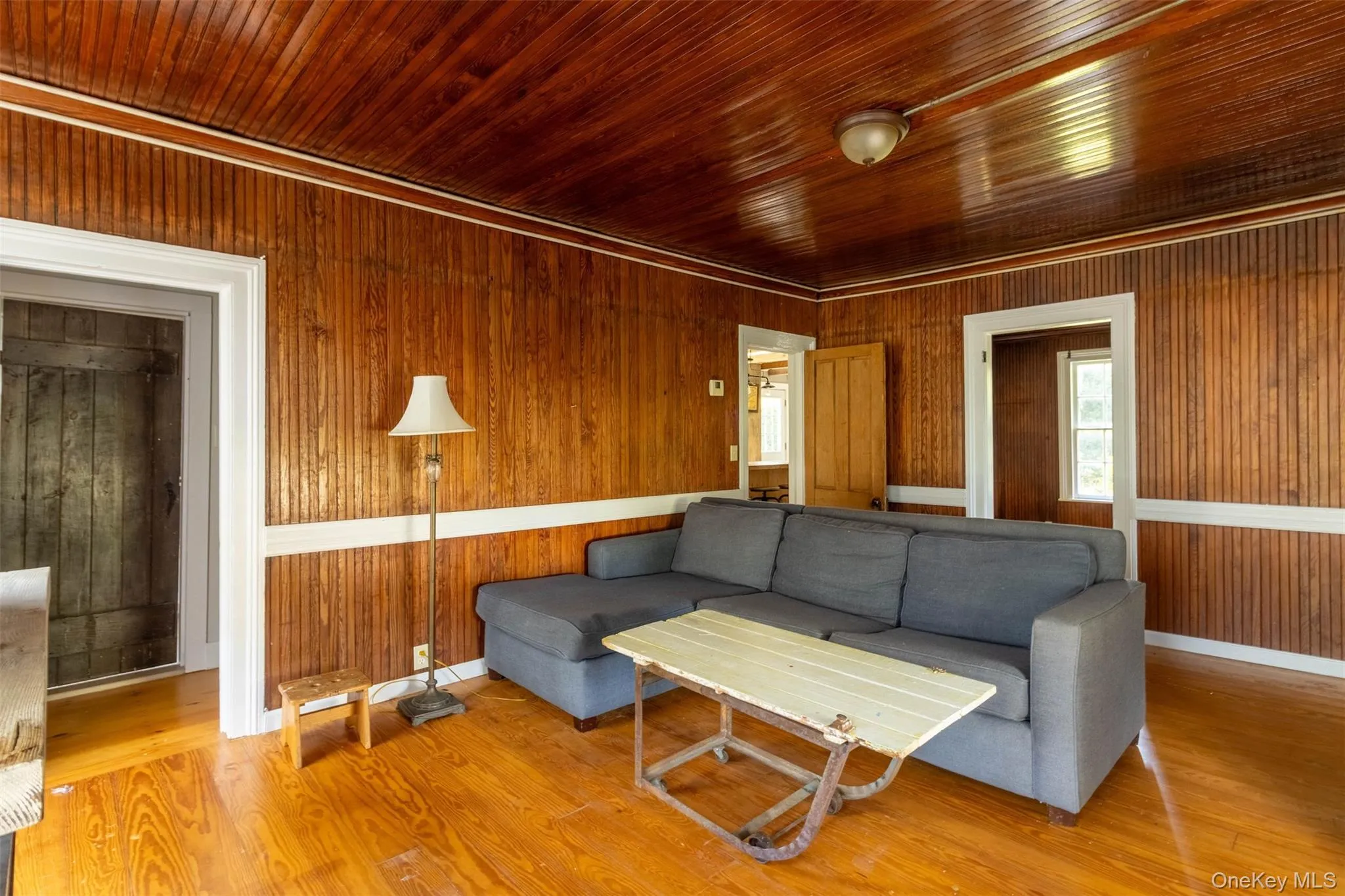 Living room with wood finished floors, wood walls, ornamental molding, and wooden ceiling Living room with wood finished floors, wood walls, ornamental molding, and wooden ceiling