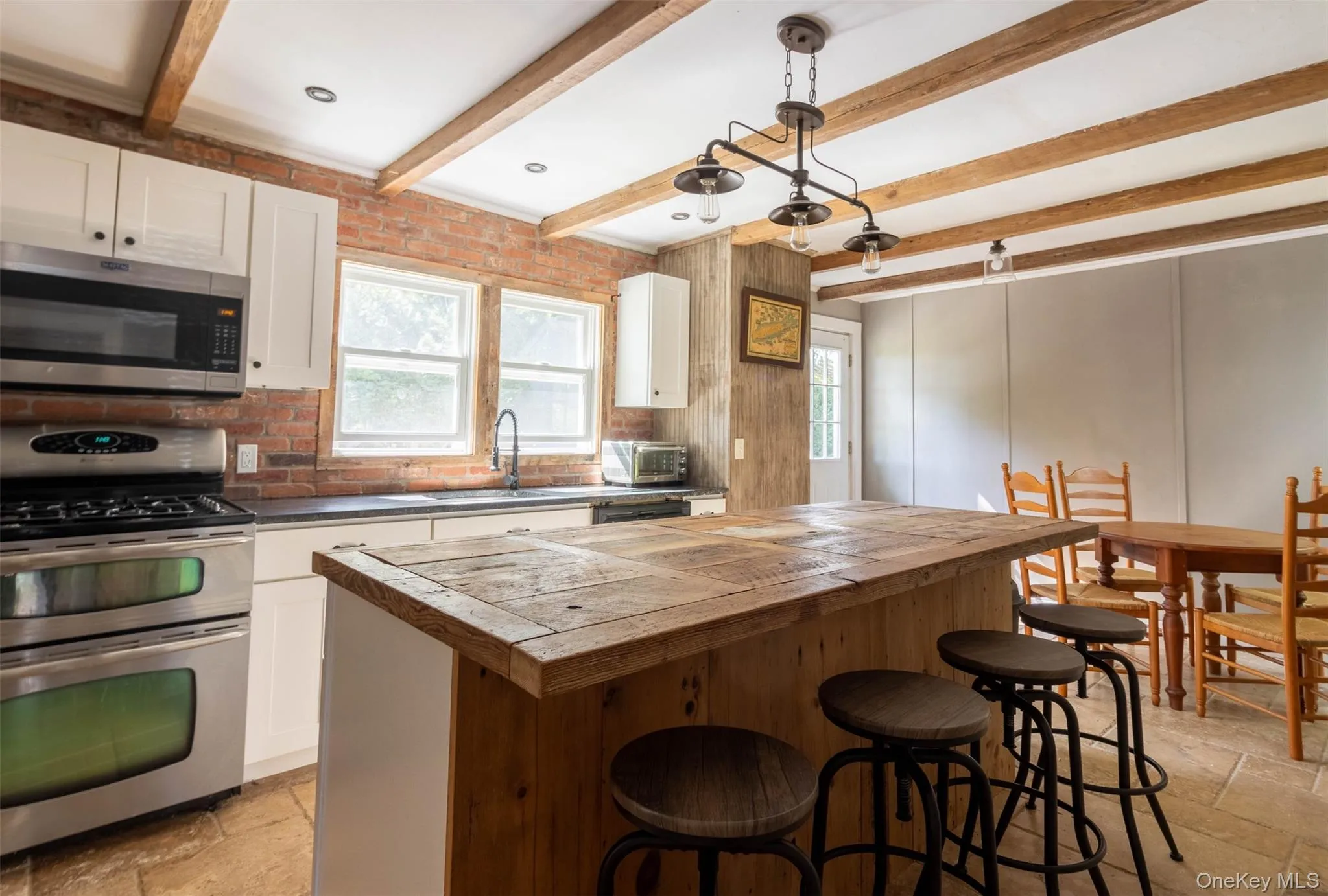 Kitchen featuring stone tile flooring, stainless steel appliances, beamed ceiling, hanging light fixtures, and a kitchen breakfast bar Kitchen featuring stone tile flooring, stainless steel appliances, beamed ceiling, hanging light fixtures, and a kitchen breakfast bar