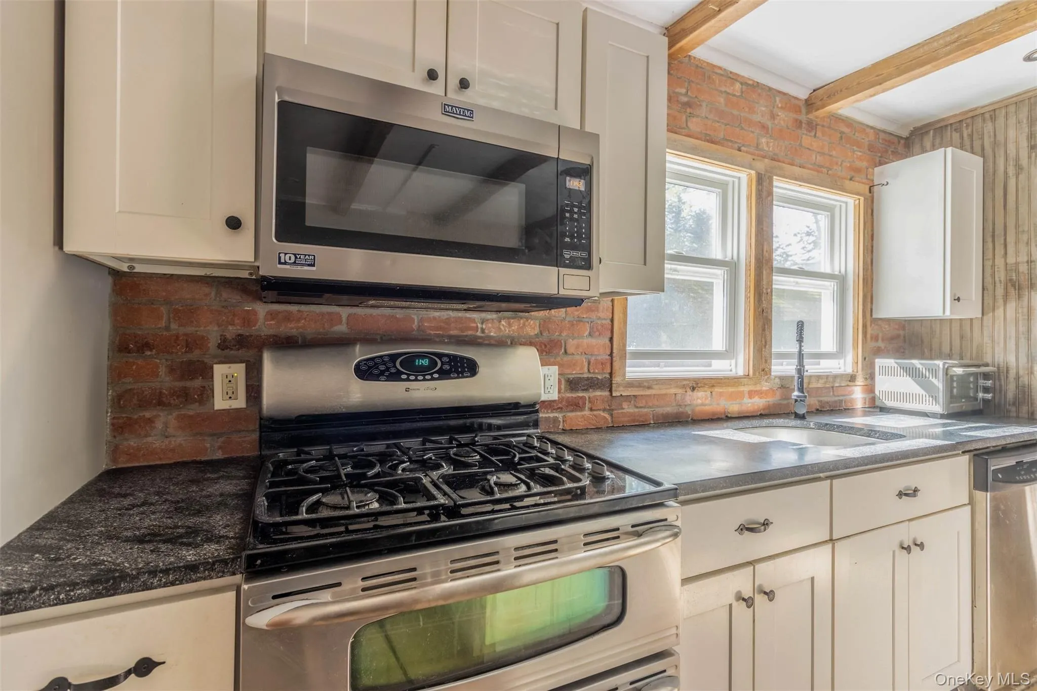 Kitchen with appliances with stainless steel finishes, beam ceiling, and decorative backsplash Kitchen with appliances with stainless steel finishes, beam ceiling, and decorative backsplash