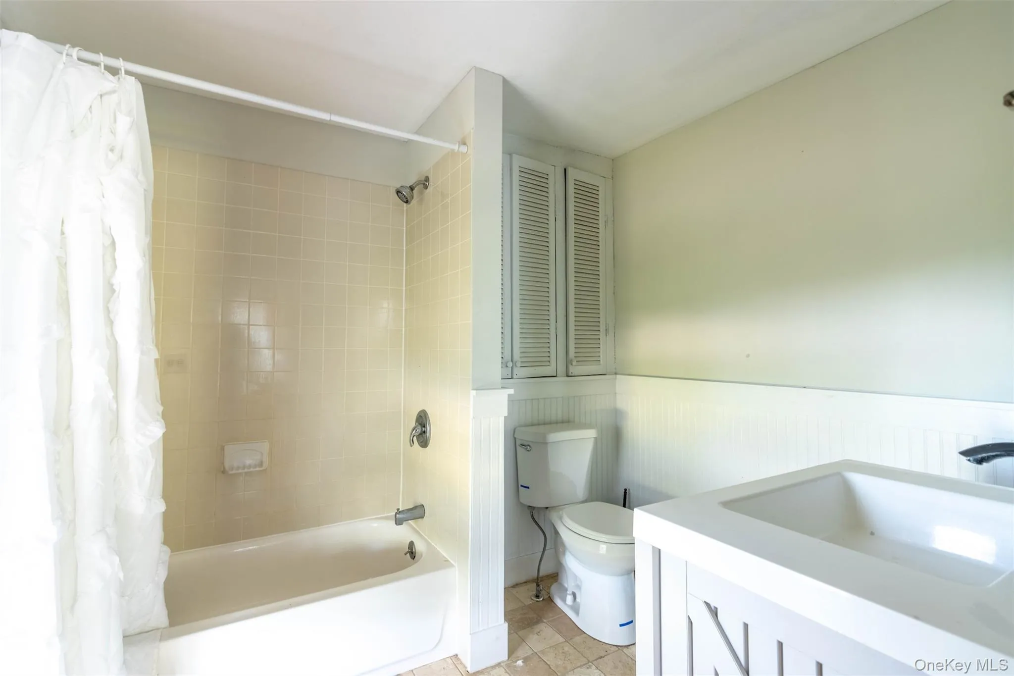 Full bathroom with shower / tub combo, vanity, wainscoting, light tile patterned flooring, and a closet Full bathroom with shower / tub combo, vanity, wainscoting, light tile patterned flooring, and a closet