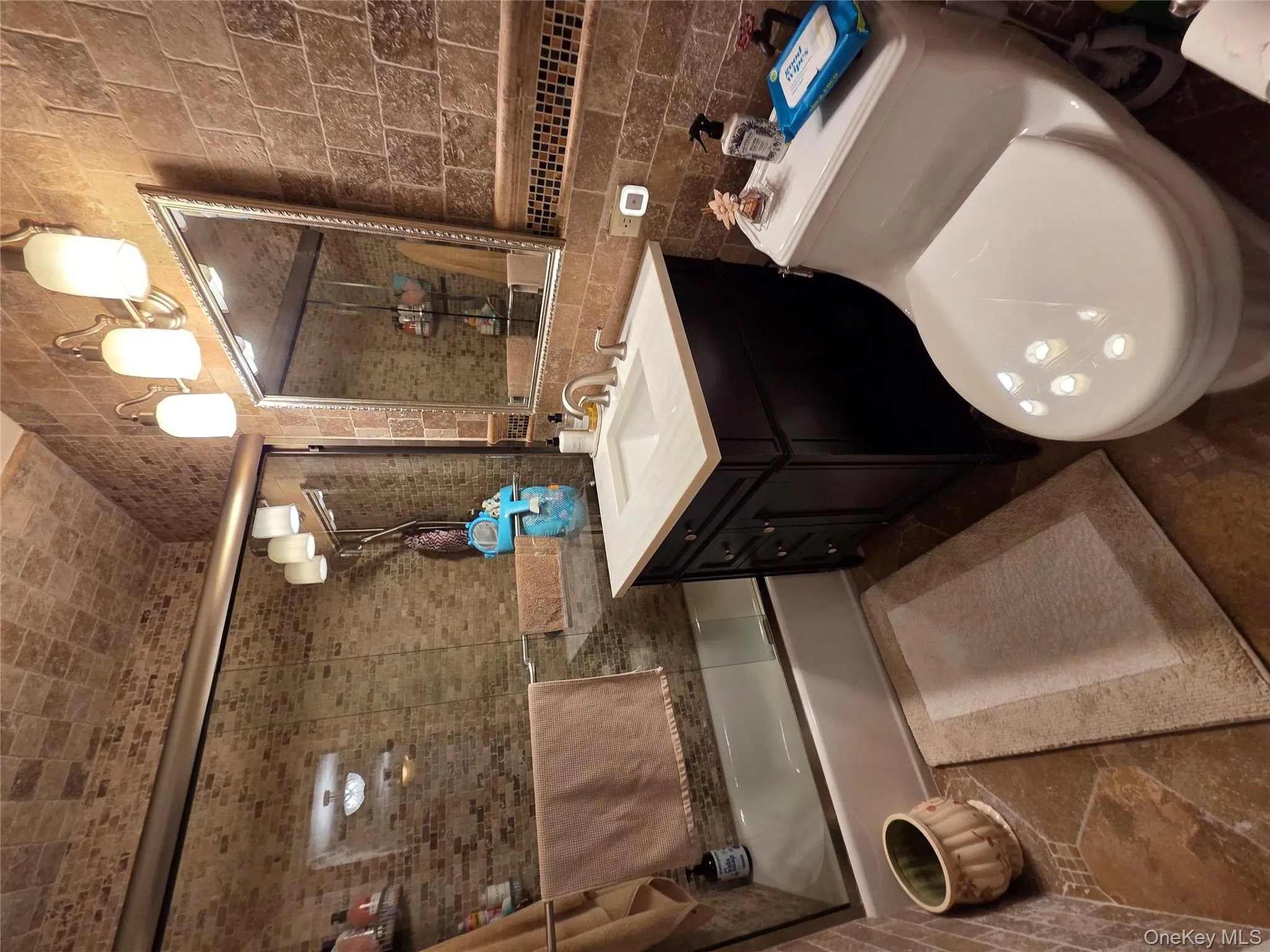 Bathroom with tile walls, vanity, bath / shower combo with glass door, and tasteful backsplash Bathroom with tile walls, vanity, bath / shower combo with glass door, and tasteful backsplash