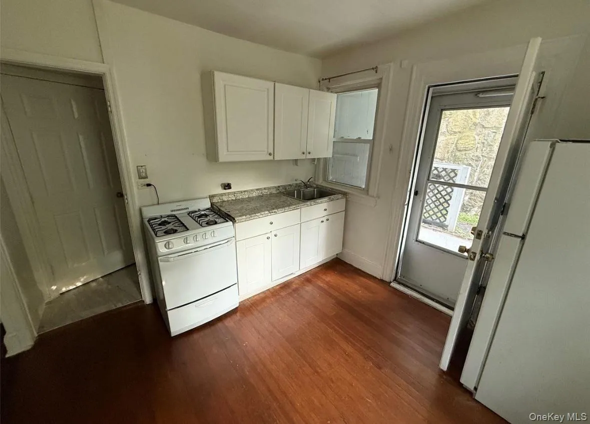 Kitchen with white appliances, white cabinets, dark wood finished floors, and light countertops Kitchen with white appliances, white cabinets, dark wood finished floors, and light countertops