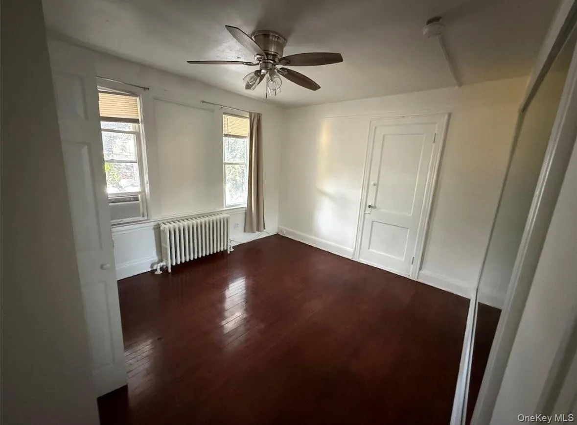Unfurnished room featuring dark wood finished floors, radiator, and a ceiling fan Unfurnished room featuring dark wood finished floors, radiator, and a ceiling fan