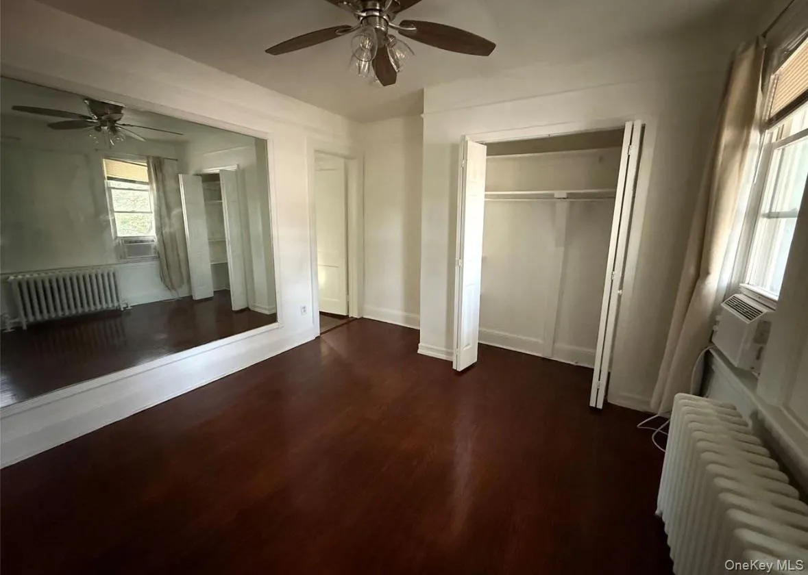 Unfurnished bedroom featuring radiator, dark wood-type flooring, ceiling fan, and cooling unit Unfurnished bedroom featuring radiator, dark wood-type flooring, ceiling fan, and cooling unit