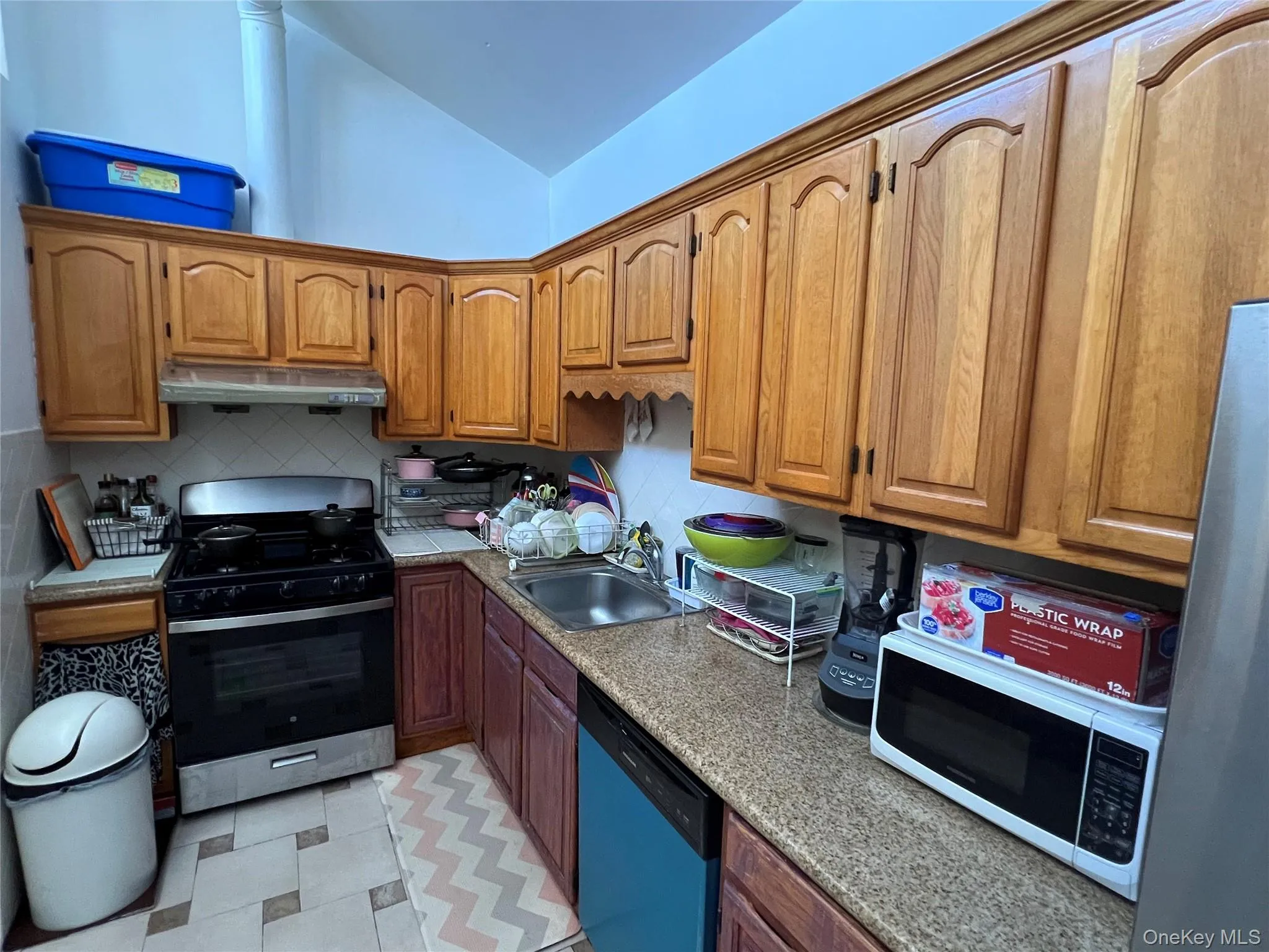 Kitchen featuring appliances with stainless steel finishes, vaulted ceiling, brown cabinets, backsplash, and under cabinet range hood Kitchen featuring appliances with stainless steel finishes, vaulted ceiling, brown cabinets, backsplash, and under cabinet range hood