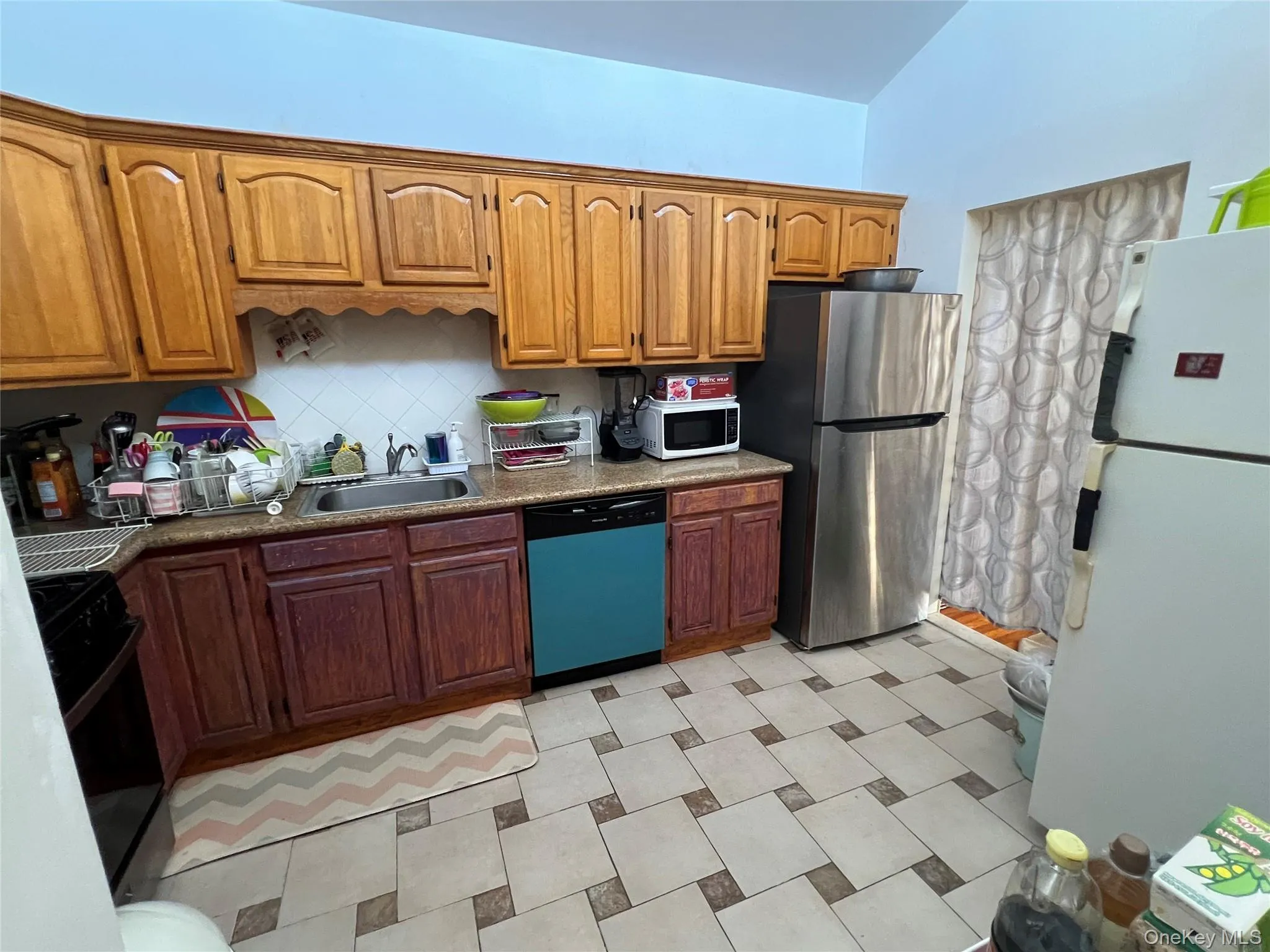 Kitchen featuring white appliances, backsplash, dark stone counters, and brown cabinets Kitchen featuring white appliances, backsplash, dark stone counters, and brown cabinets