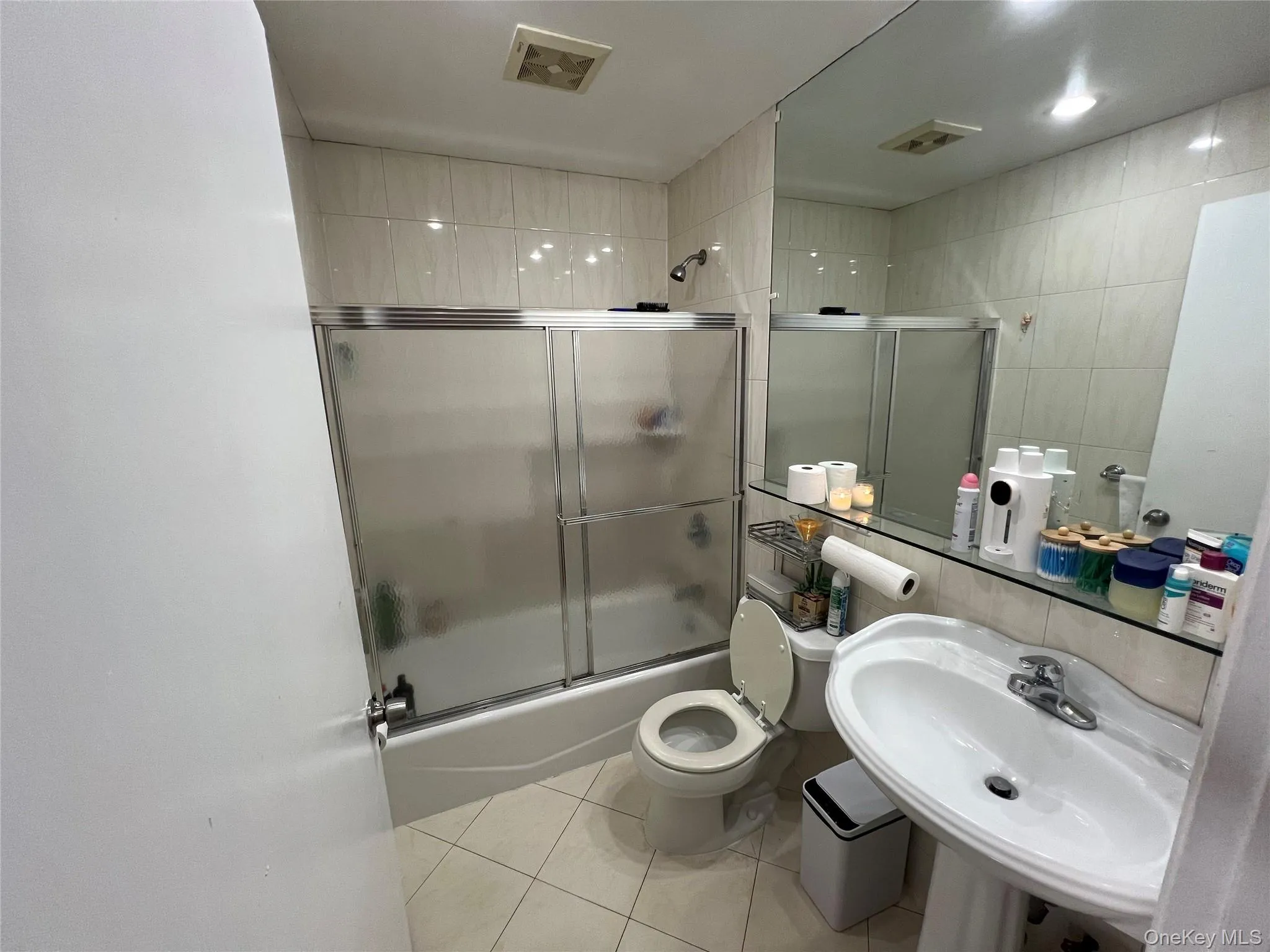Bathroom featuring bath / shower combo with glass door, light tile patterned flooring, and tile walls Bathroom featuring bath / shower combo with glass door, light tile patterned flooring, and tile walls