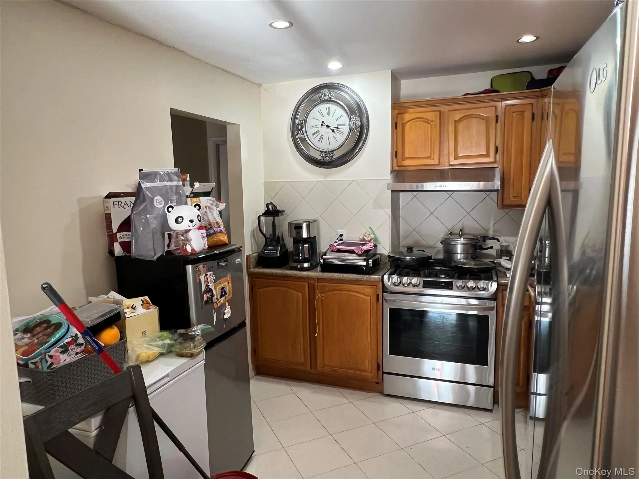 Kitchen featuring appliances with stainless steel finishes, backsplash, light tile patterned floors, brown cabinetry, and under cabinet range hood Kitchen featuring appliances with stainless steel finishes, backsplash, light tile patterned floors, brown cabinetry, and under cabinet range hood