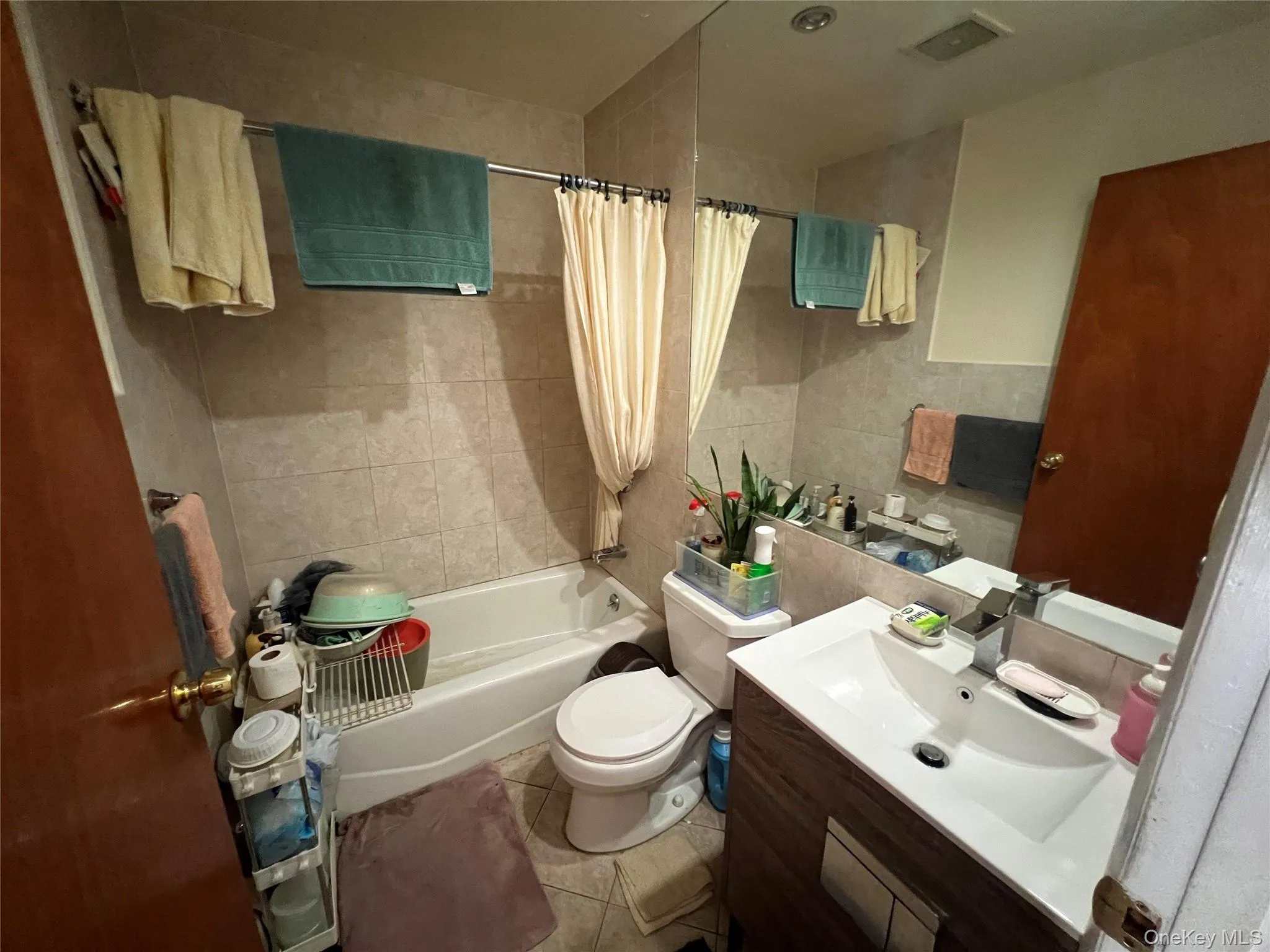 Full bath with shower / bath combo, light tile patterned flooring, vanity, and tile walls Full bath with shower / bath combo, light tile patterned flooring, vanity, and tile walls