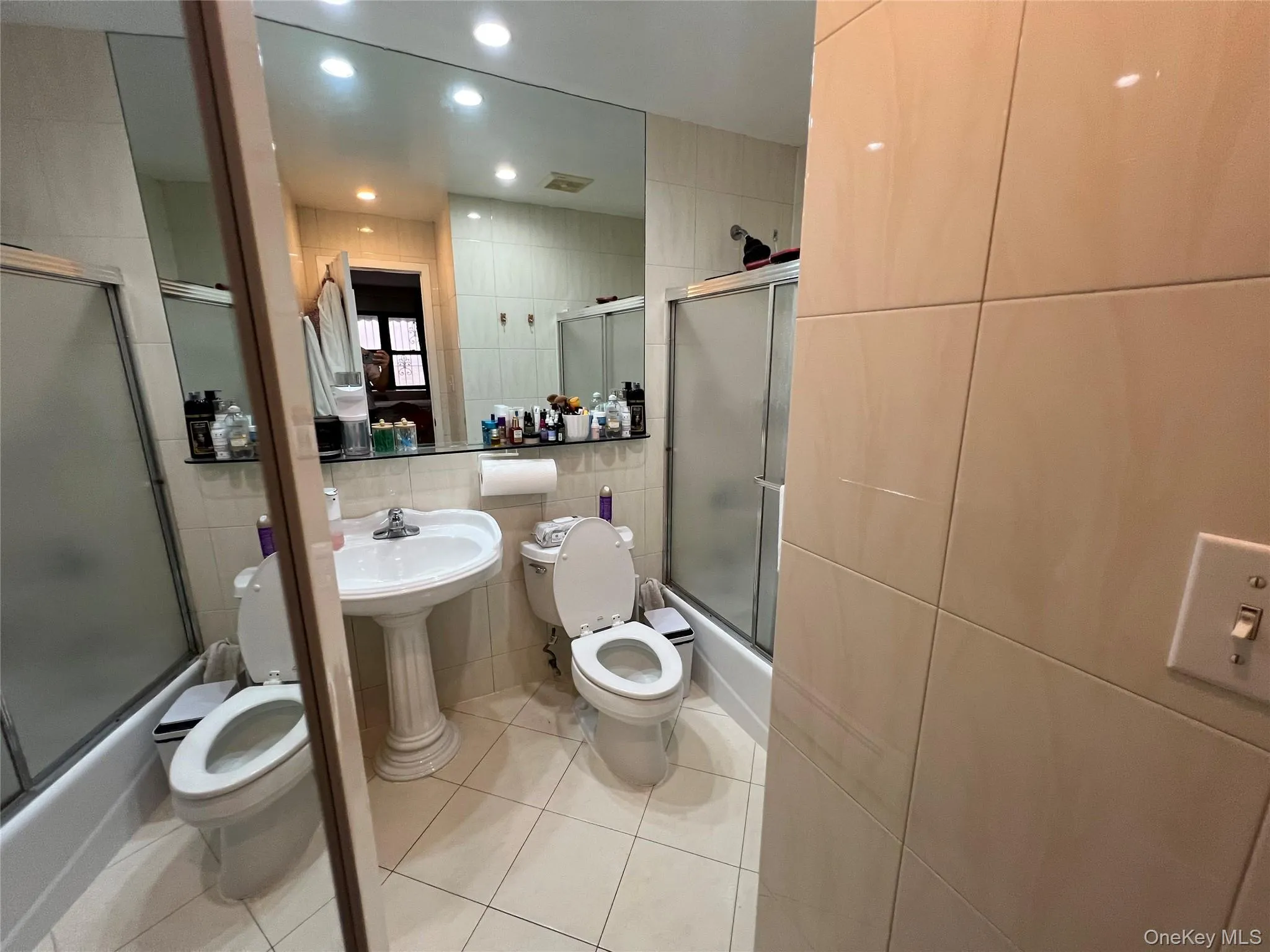 Full bath featuring tile walls, shower / bath combination with glass door, light tile patterned floors, and recessed lighting Full bath featuring tile walls, shower / bath combination with glass door, light tile patterned floors, and recessed lighting