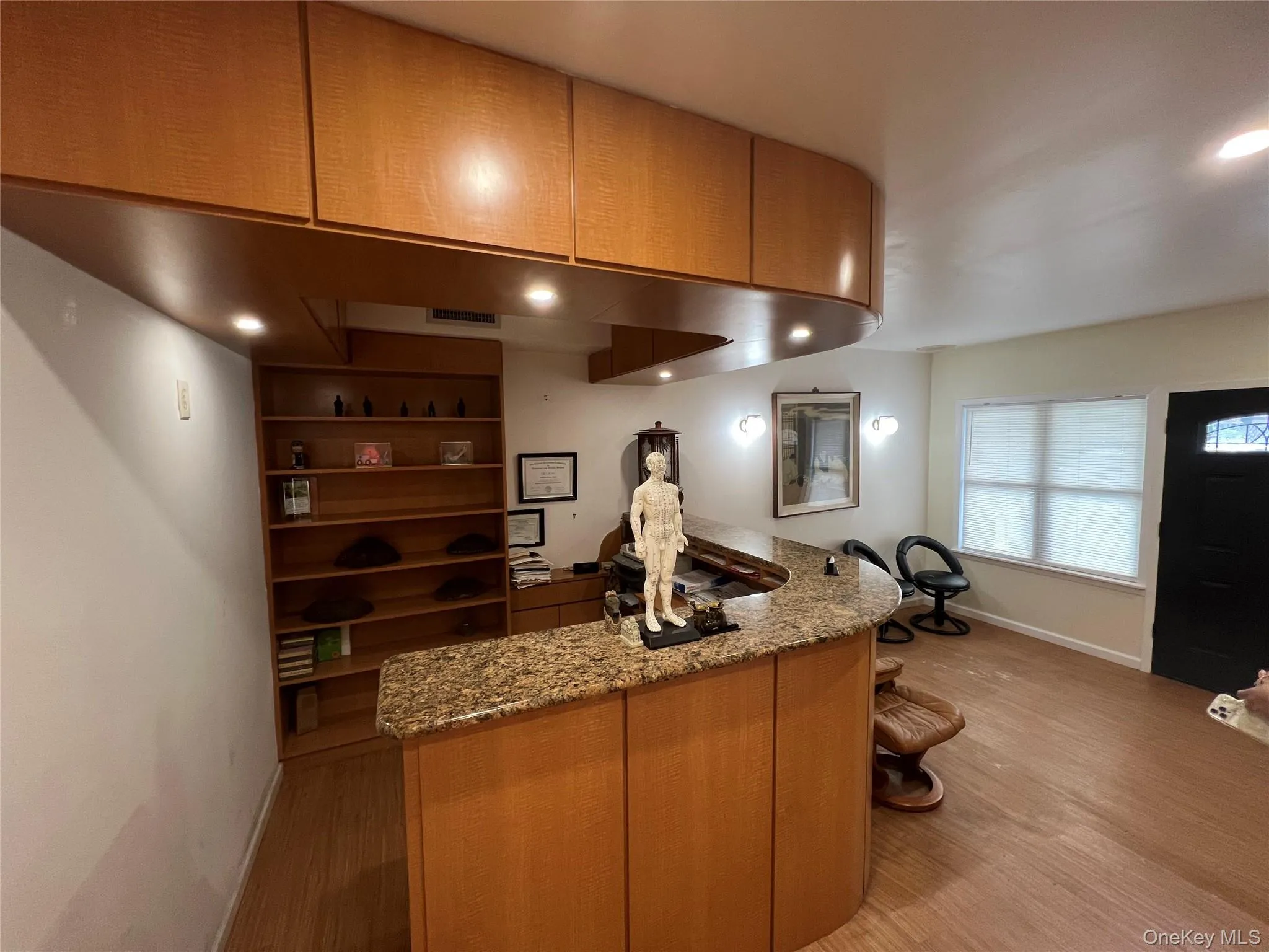 Kitchen with light stone countertops, light wood-style flooring, open shelves, brown cabinetry, and recessed lighting Kitchen with light stone countertops, light wood-style flooring, open shelves, brown cabinetry, and recessed lighting