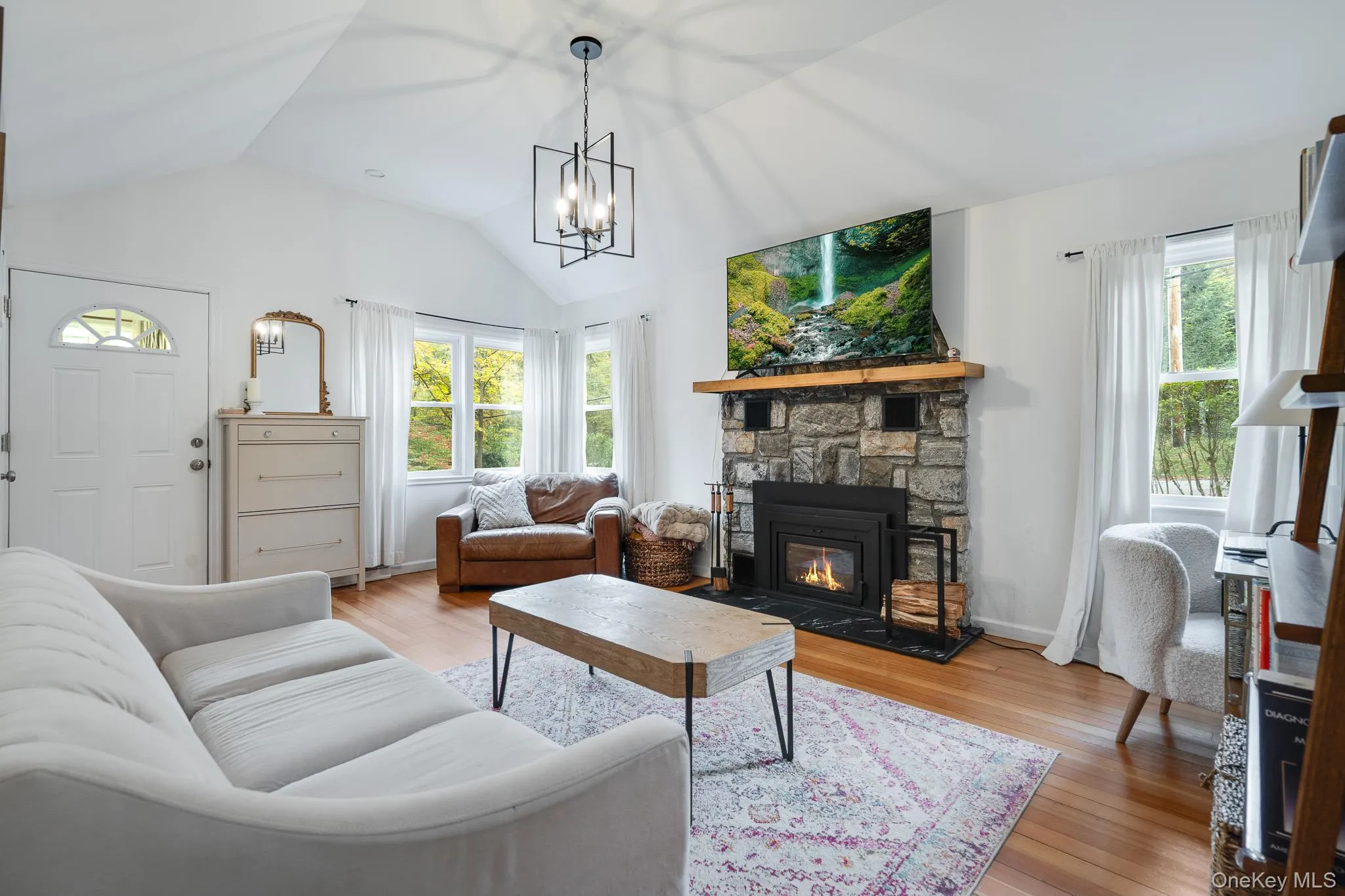 Living area featuring light wood-type flooring, vaulted ceiling, a stone fireplace, and a chandelier Living area featuring light wood-type flooring, vaulted ceiling, a stone fireplace, and a chandelier