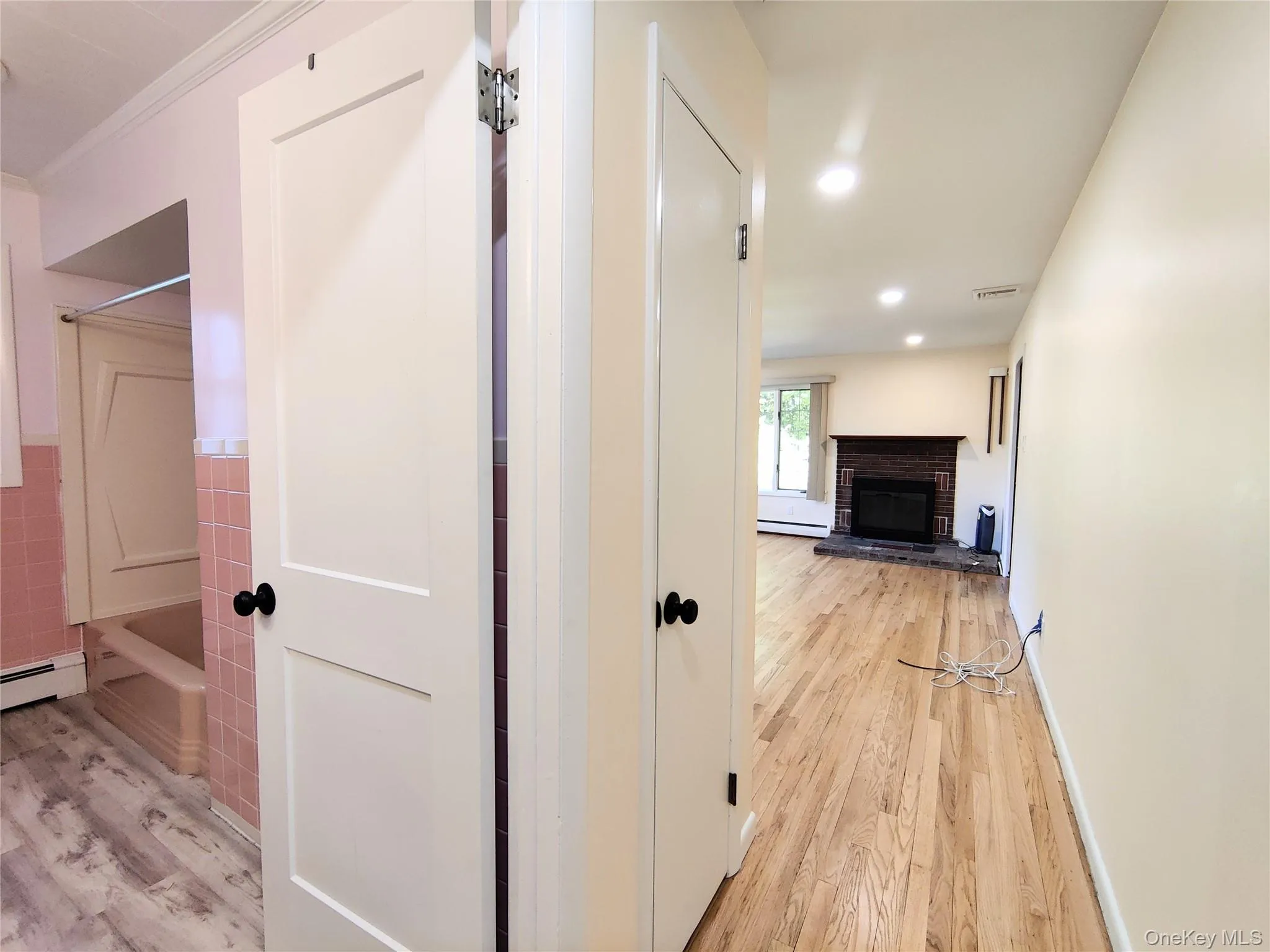 Corridor featuring light wood-type flooring, recessed lighting, tile walls, and a baseboard heating unit Corridor featuring light wood-type flooring, recessed lighting, tile walls, and a baseboard heating unit