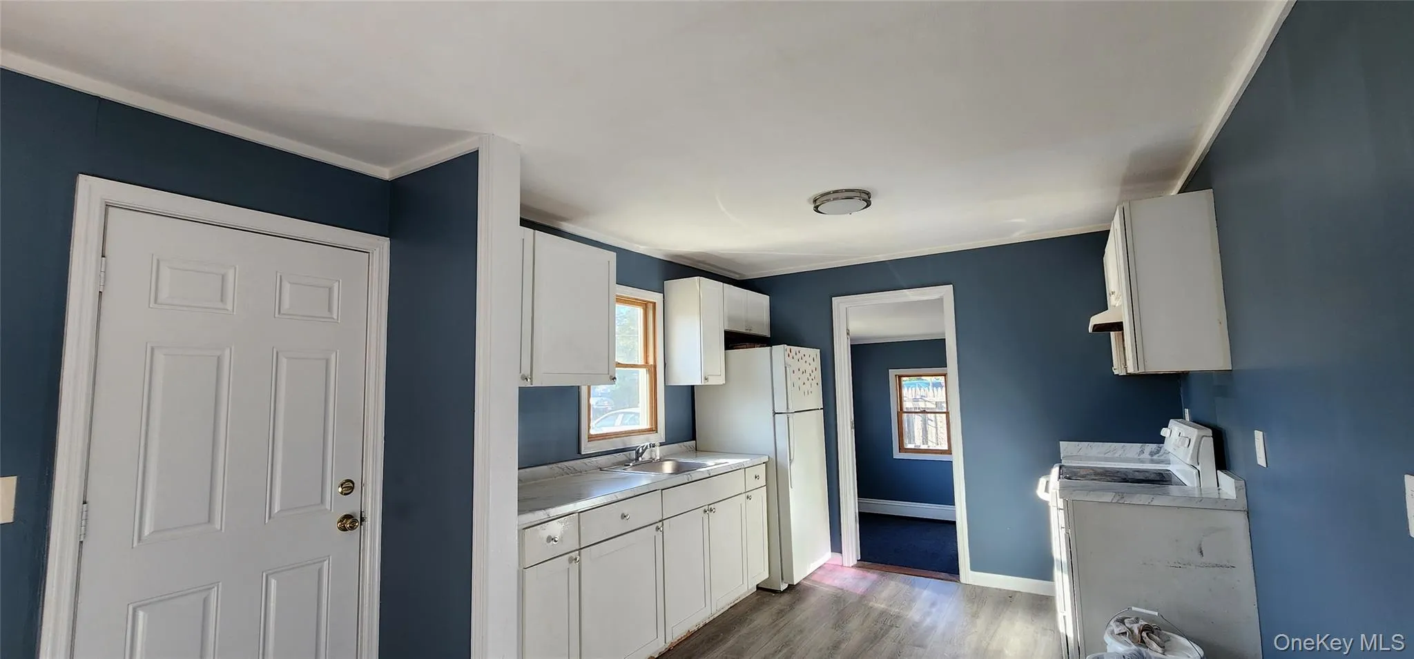 Kitchen with white appliances, dark wood-style floors, light countertops, white cabinets, and crown molding Kitchen with white appliances, dark wood-style floors, light countertops, white cabinets, and crown molding